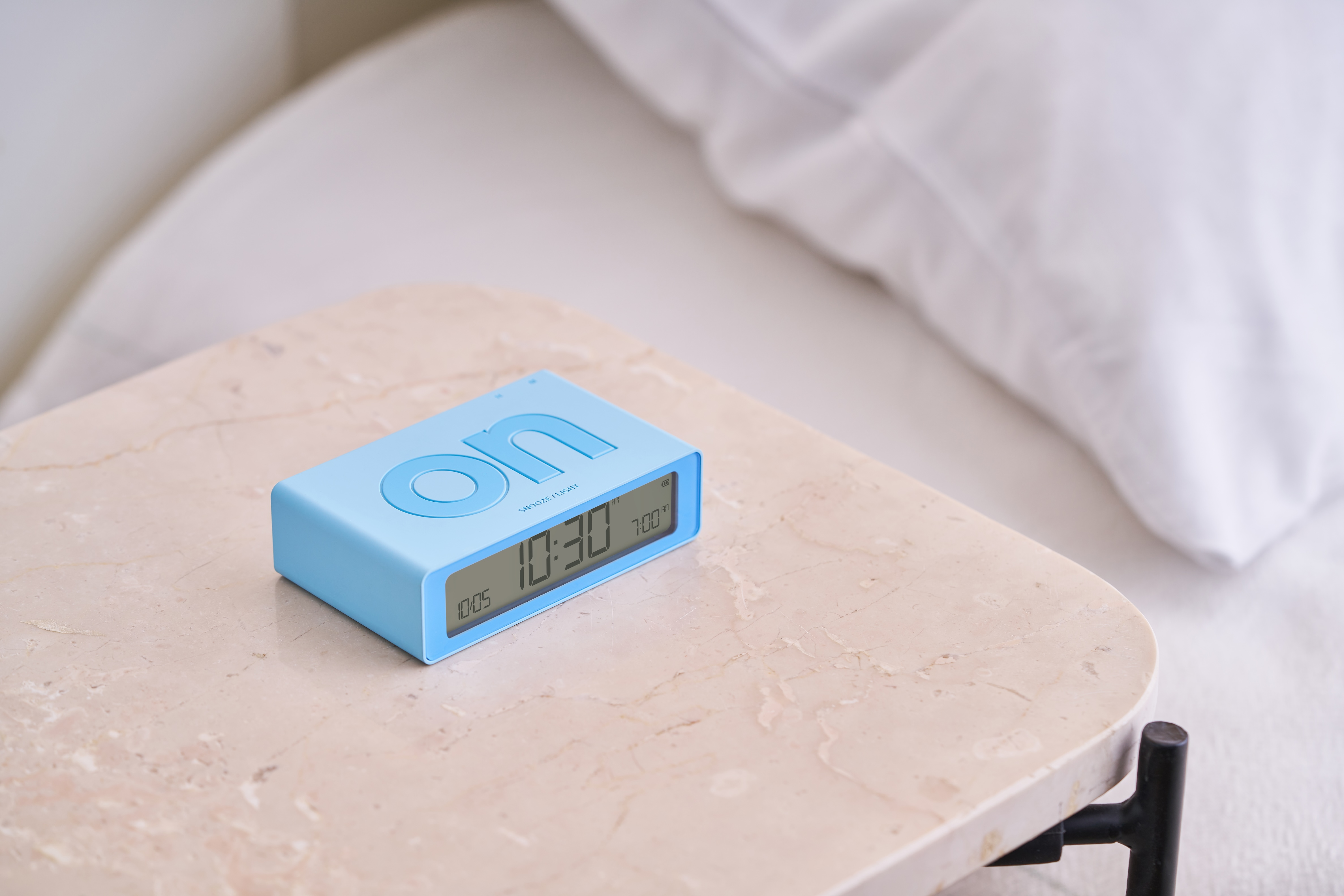 Una sveglia digitale blu con la scritta "on". È su un tavolo di marmo.