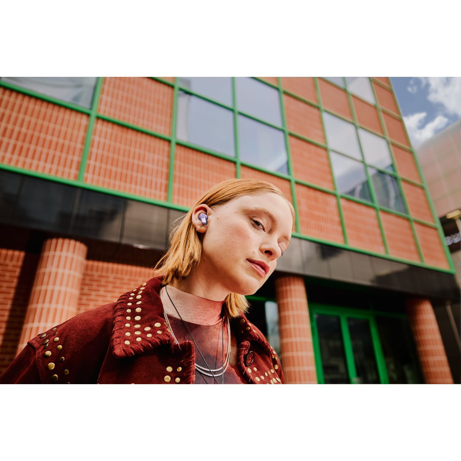 A woman with purple earbuds in her ears, standing in front of a building.
