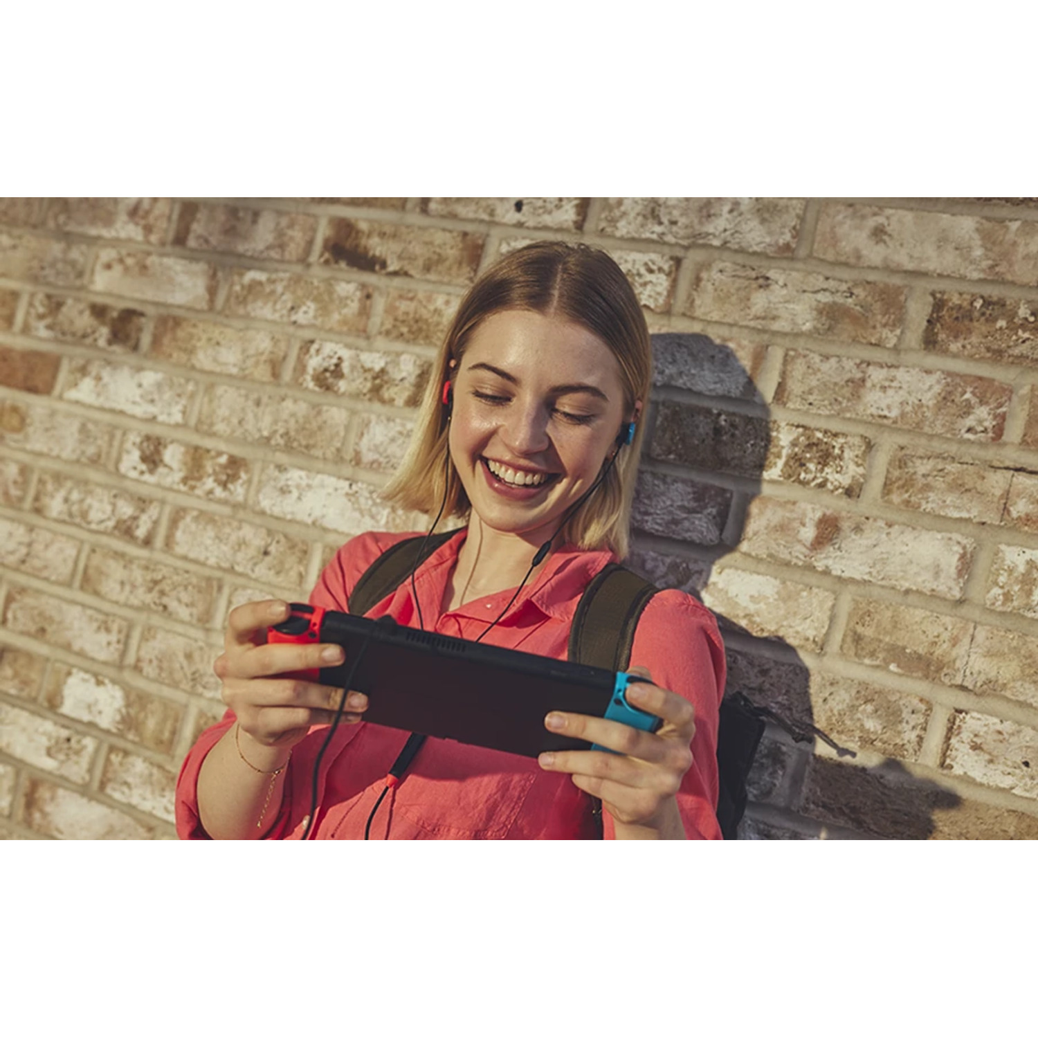 Une femme souriante joue à un jeu portable, fond de mur de briques.