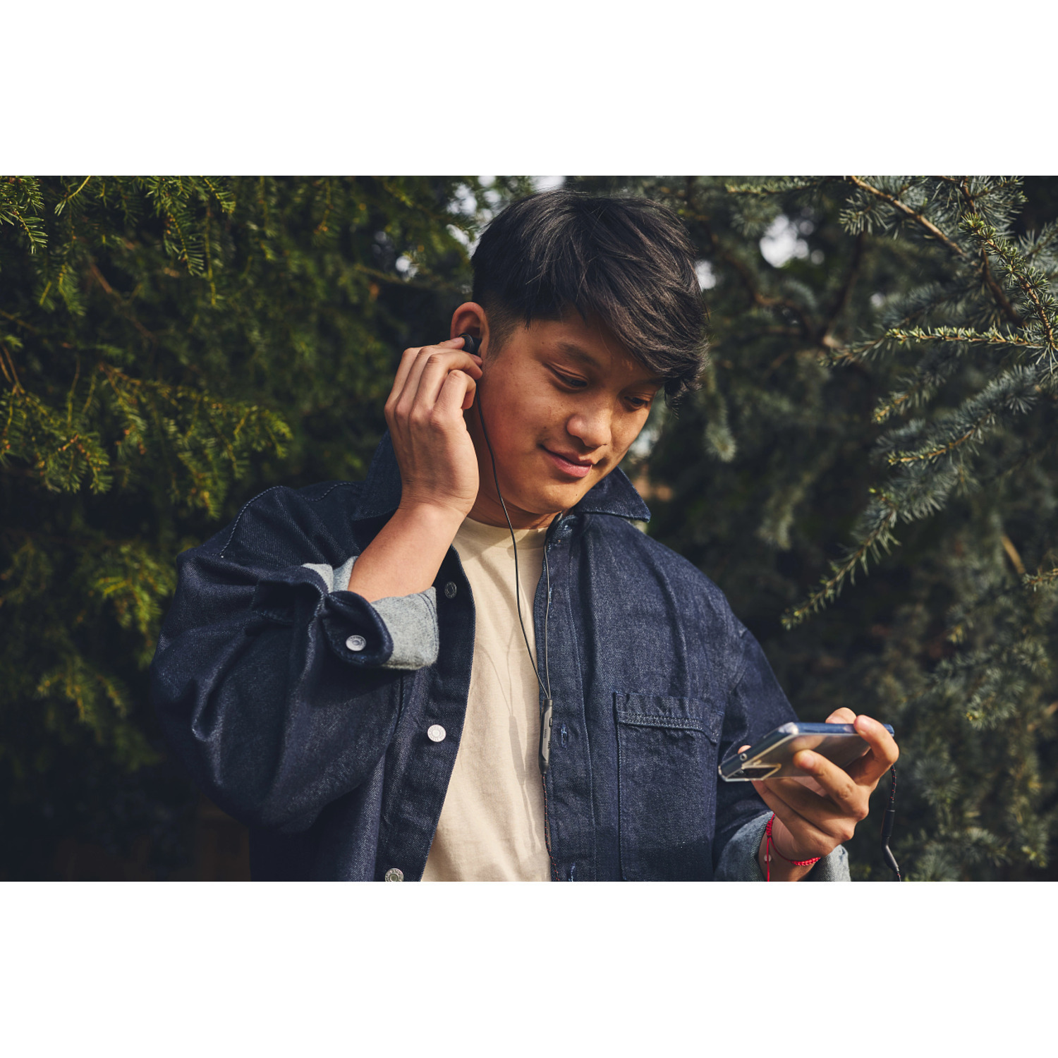 Jeune homme écoutant de la musique avec des écouteurs. Il tient un téléphone. Fond vert.