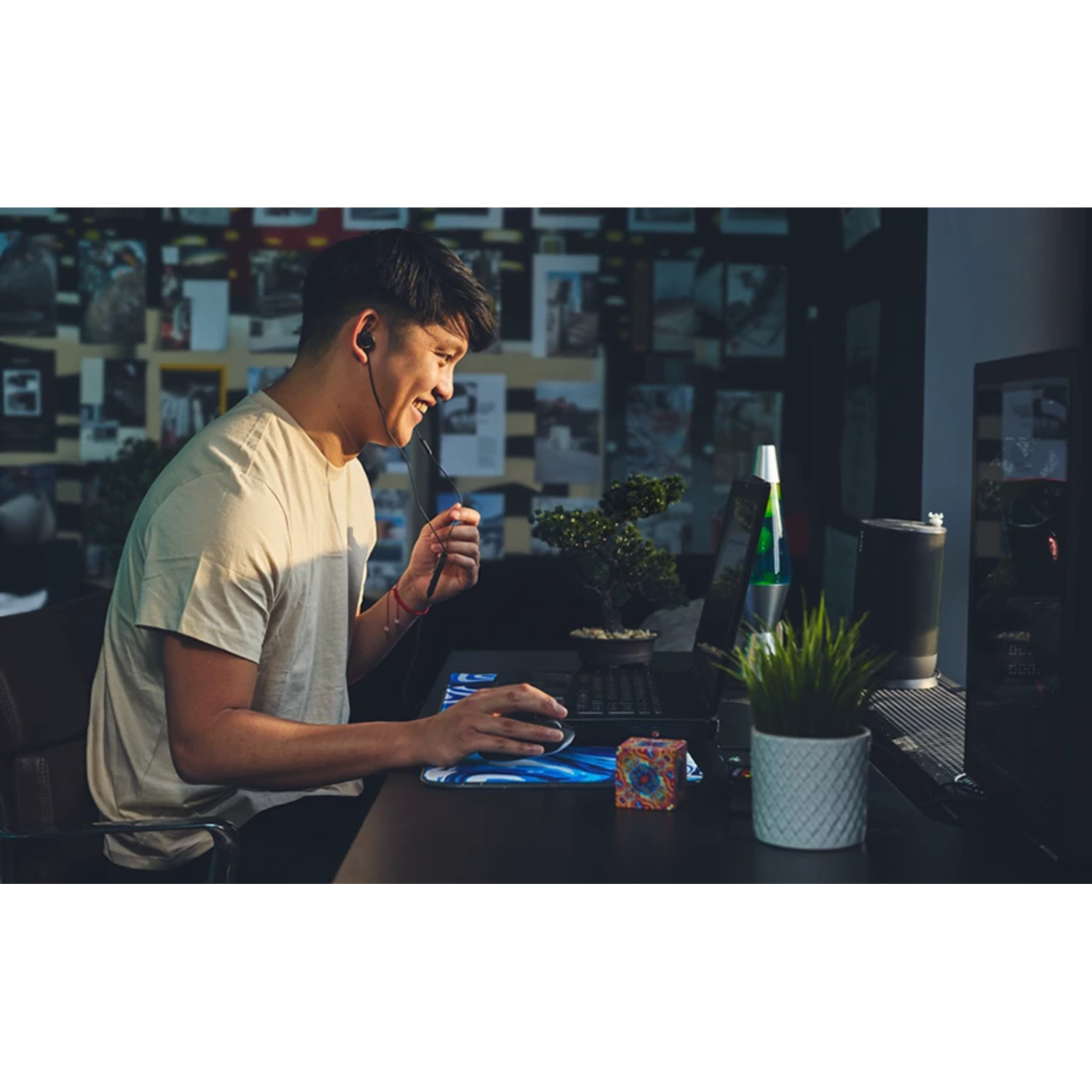 Un homme en chemise beige assis à un bureau, souriant en utilisant un ordinateur avec un casque.