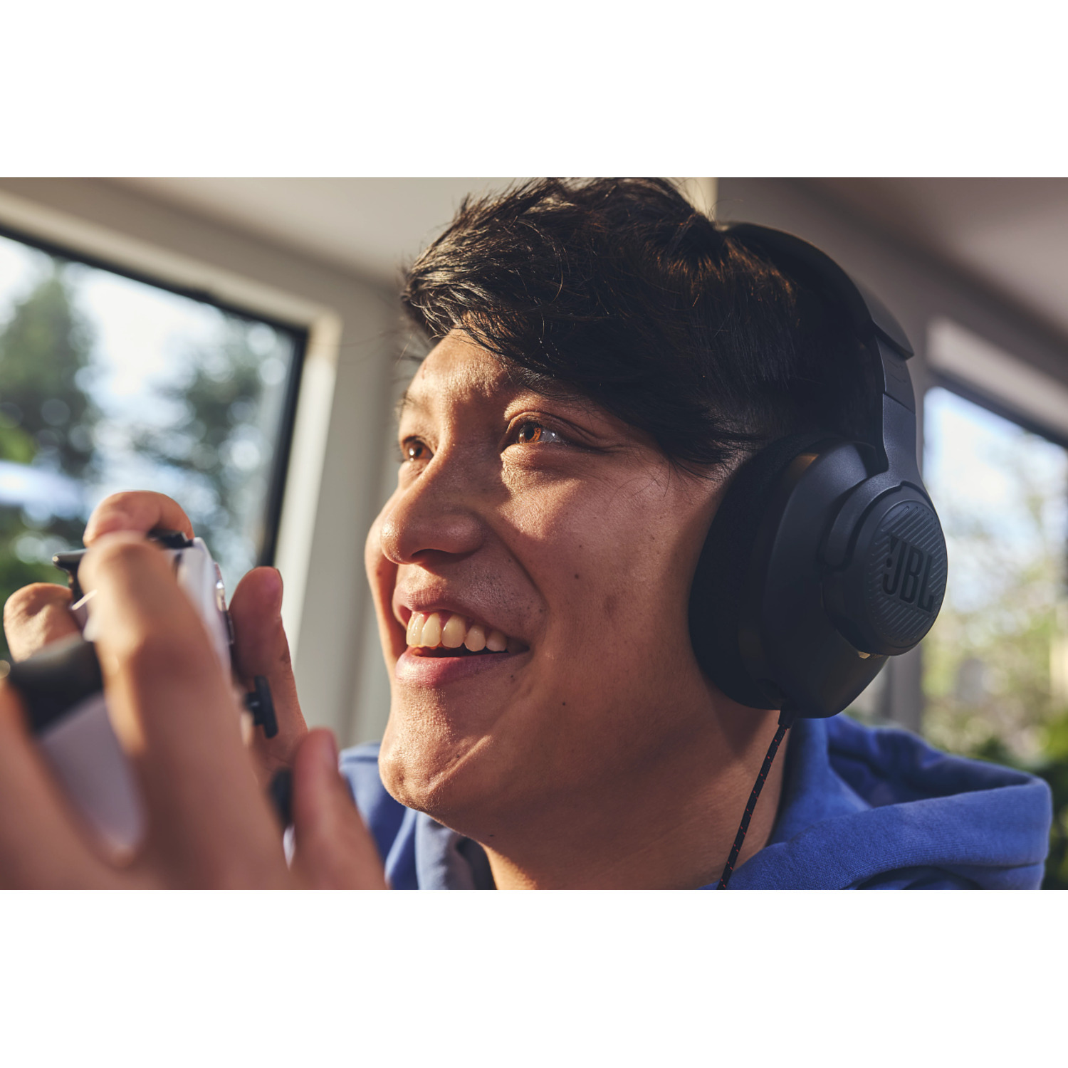 A man wearing black JBL headphones, smiling while playing a video game.