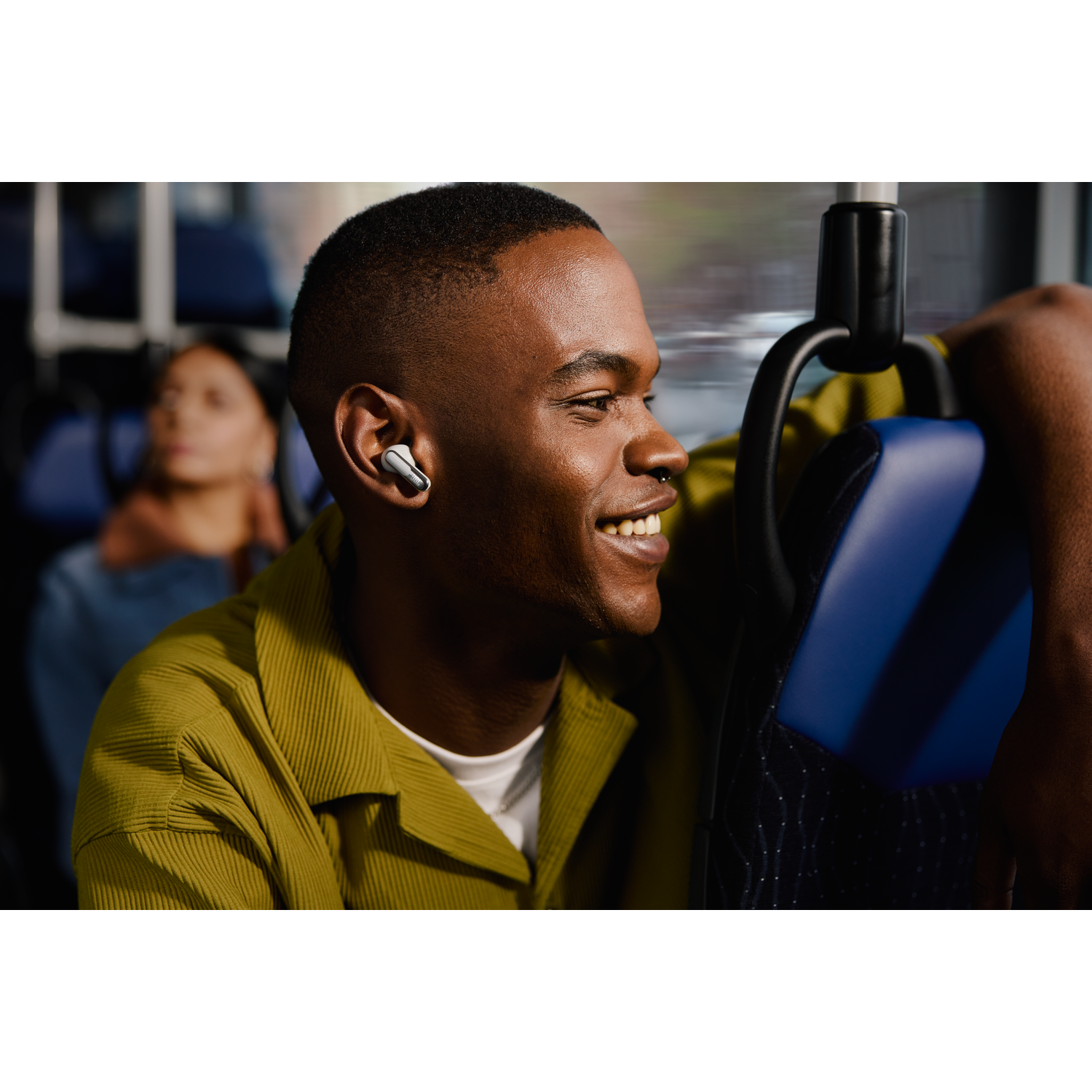 Man on a bus wearing earbuds, smiling. Background of bus interior.