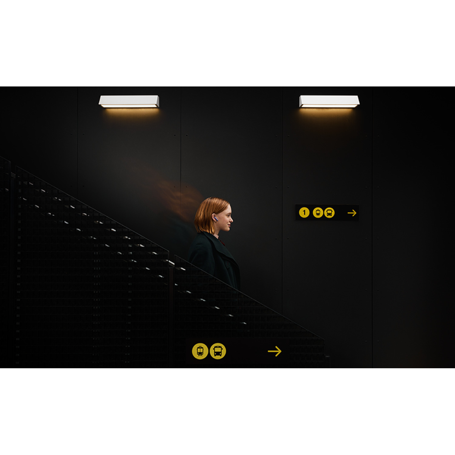 A woman walks up stairs, passing a sign with bus and train symbols.