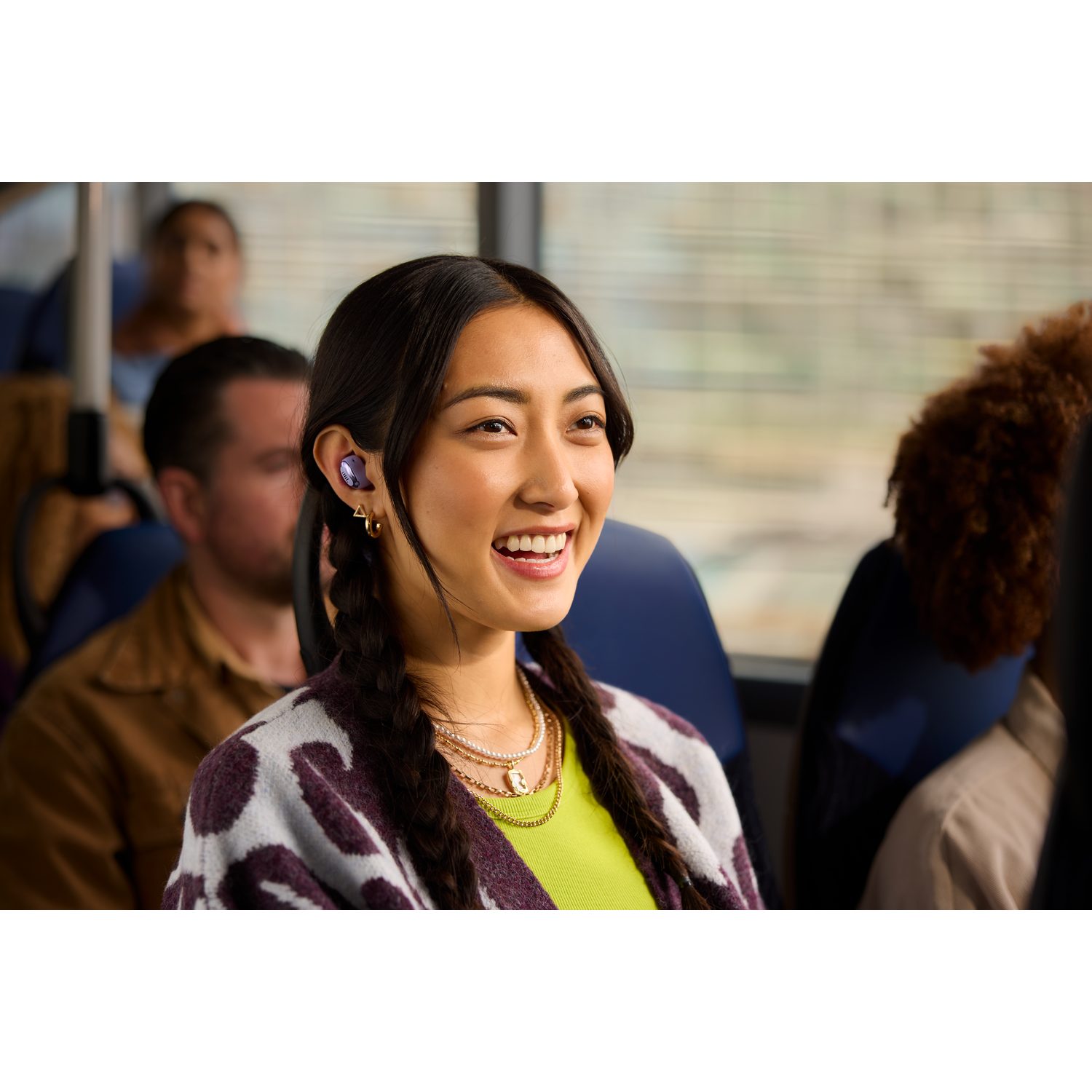 Femme avec des tresses souriant dans le bus, portant des écouteurs. Autres en arrière-plan.