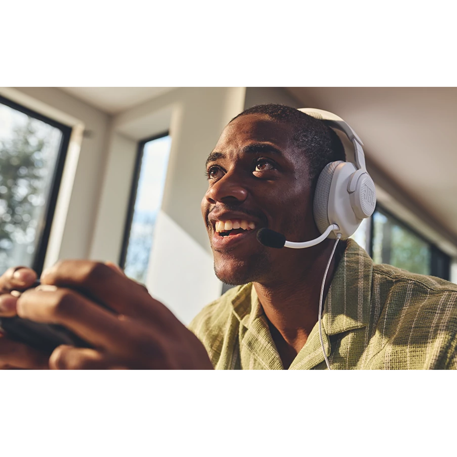 Man wearing white JBL headphones. He is smiling and holding a controller. Bright, indoor setting.