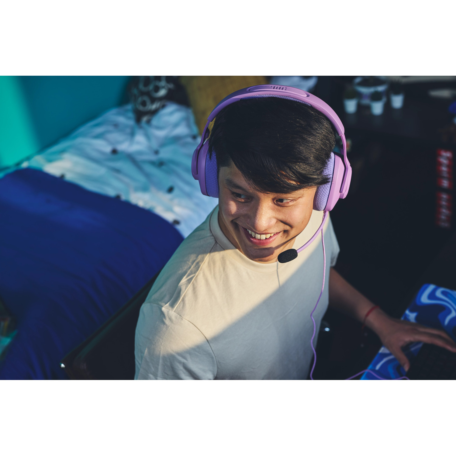 A man wearing purple headphones smiles while gaming. The background is blurred.