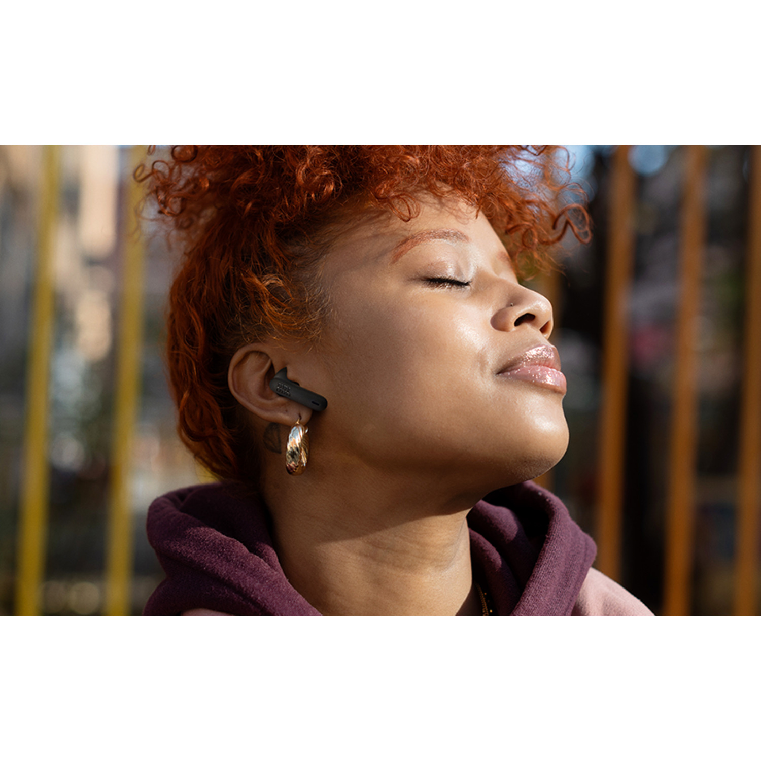 Woman with earbuds in her ears, eyes closed, enjoying the sun.