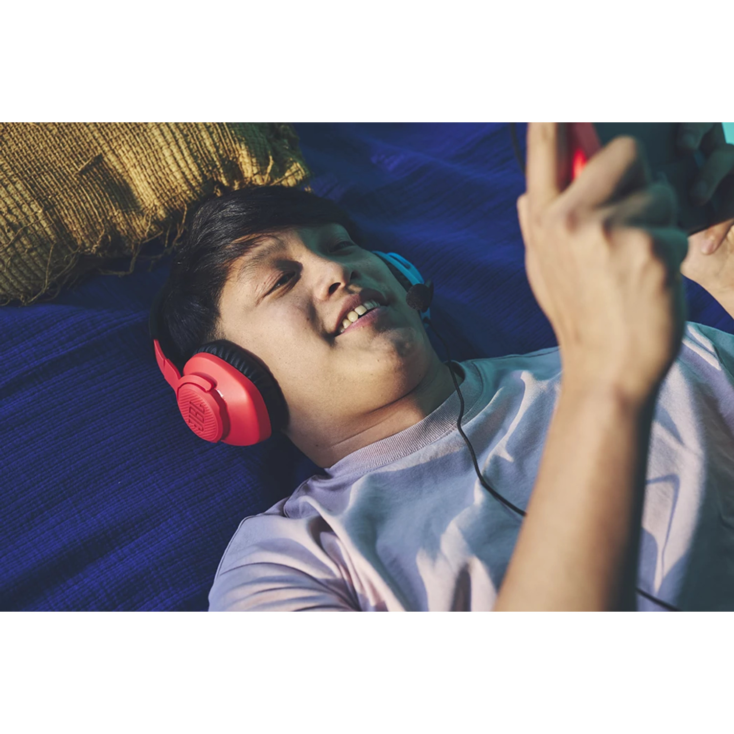 Man lying down, wearing red headphones, playing on a tablet. He smiles while looking at the screen.