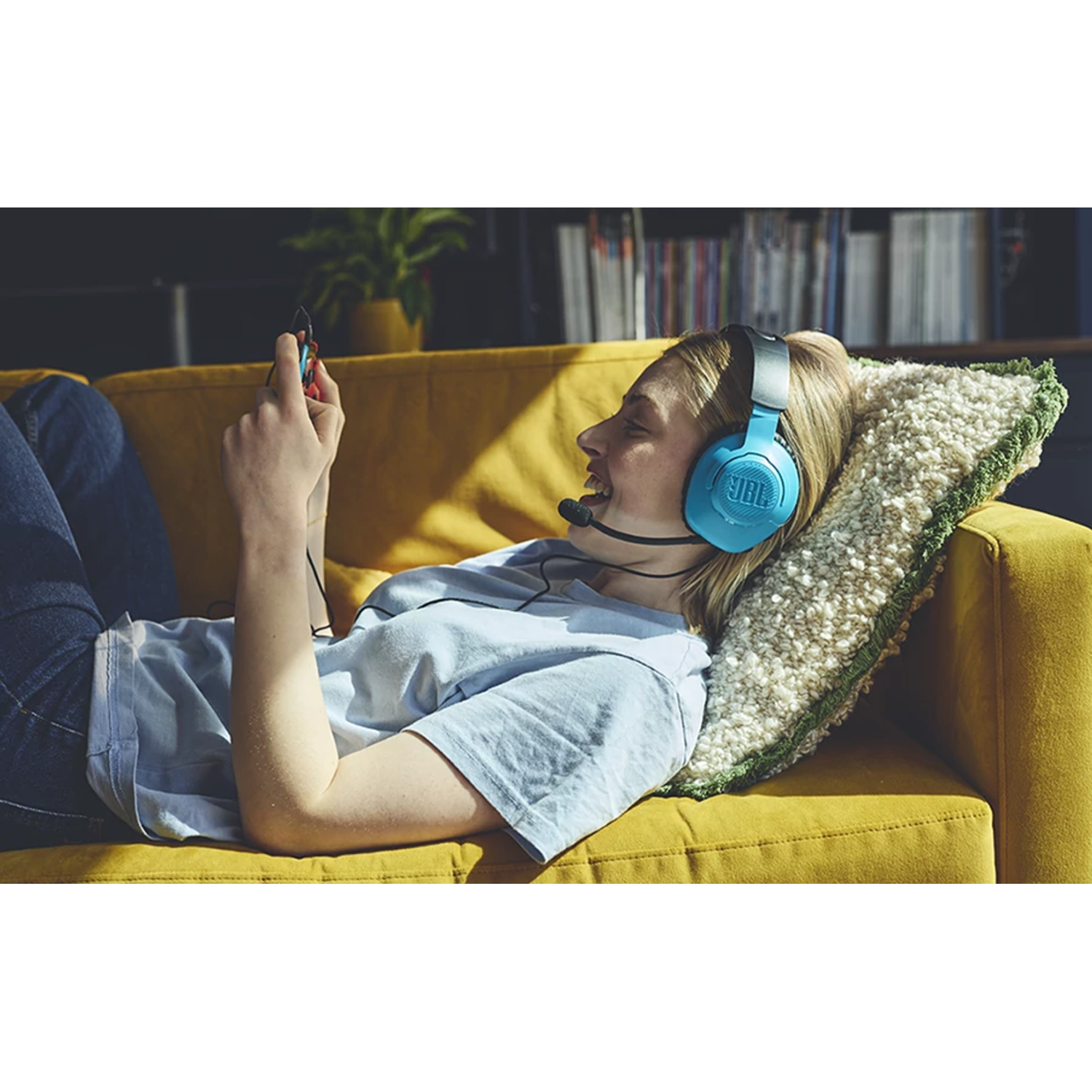 A person lying on a yellow couch wearing blue headphones is looking at a phone.