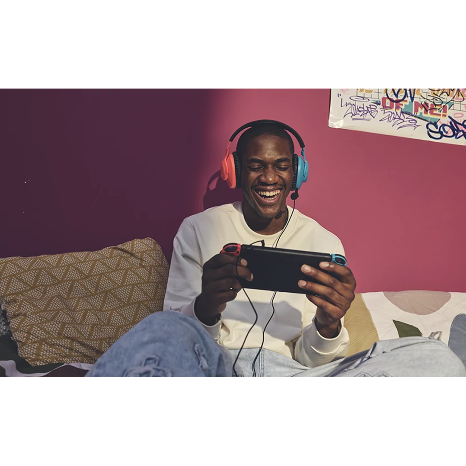 A person is smiling and playing a game on a handheld device while wearing headphones.