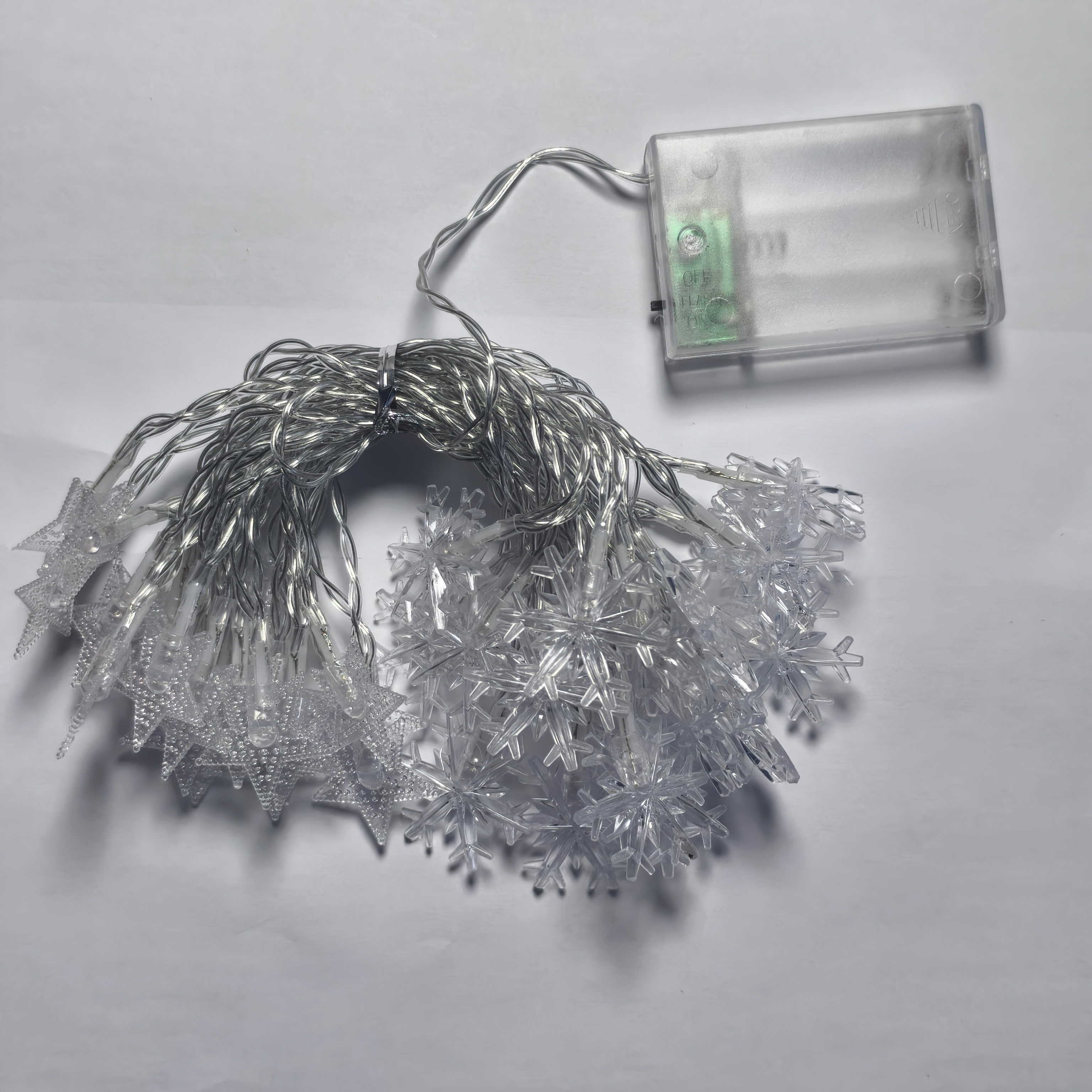 Szereg światełek w kształcie płatków śniegu z pojemnikiem na baterie na białym tle.