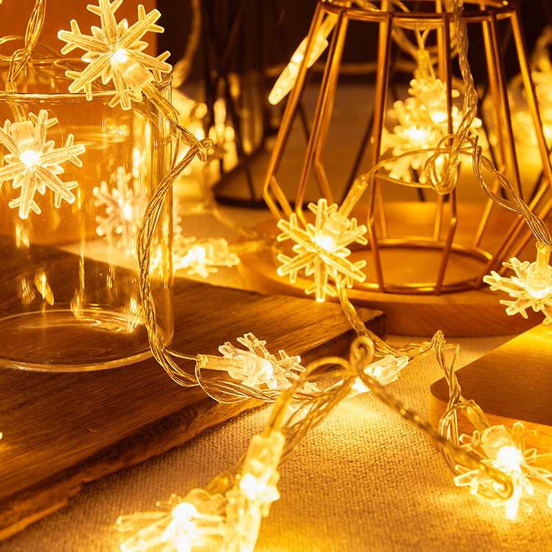 Lampki choinkowe z dekoracjami w kształcie płatków śniegu na drewnianej desce, obok złotej klatki.