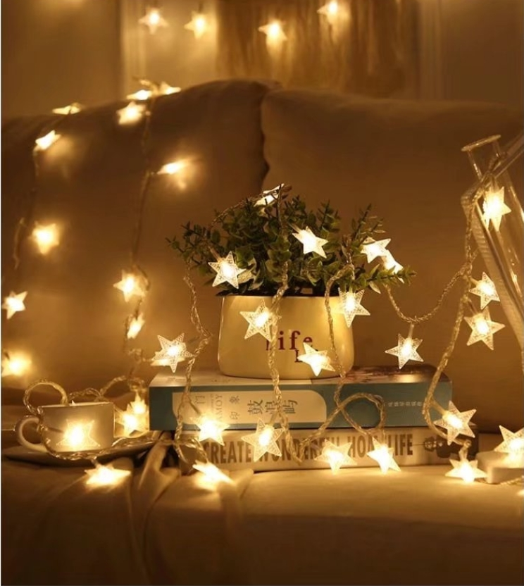 Światła łańcuchowe w kształcie gwiazd, nad łóżkiem z poduszkami, filiżanką i książkami.