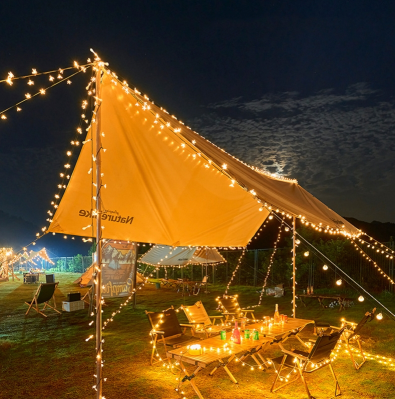 Scena kempingowa w nocy z oświetleniem rozwieszonym na namiocie.