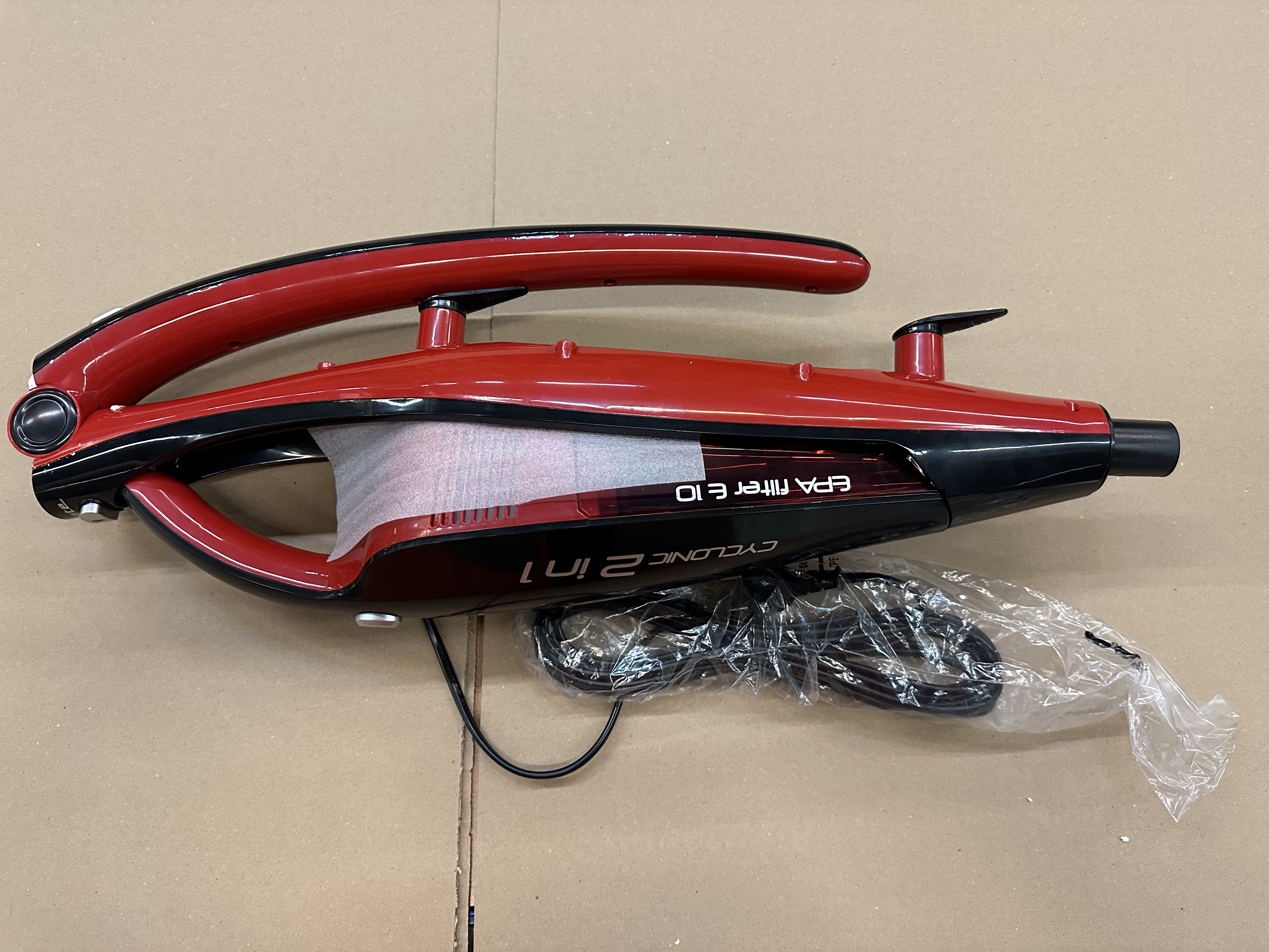 Czerwono-czarny odkurzacz ręczny na brązowej powierzchni. Widoczna jest marka 'CYCLONIC 2 IN 1'.