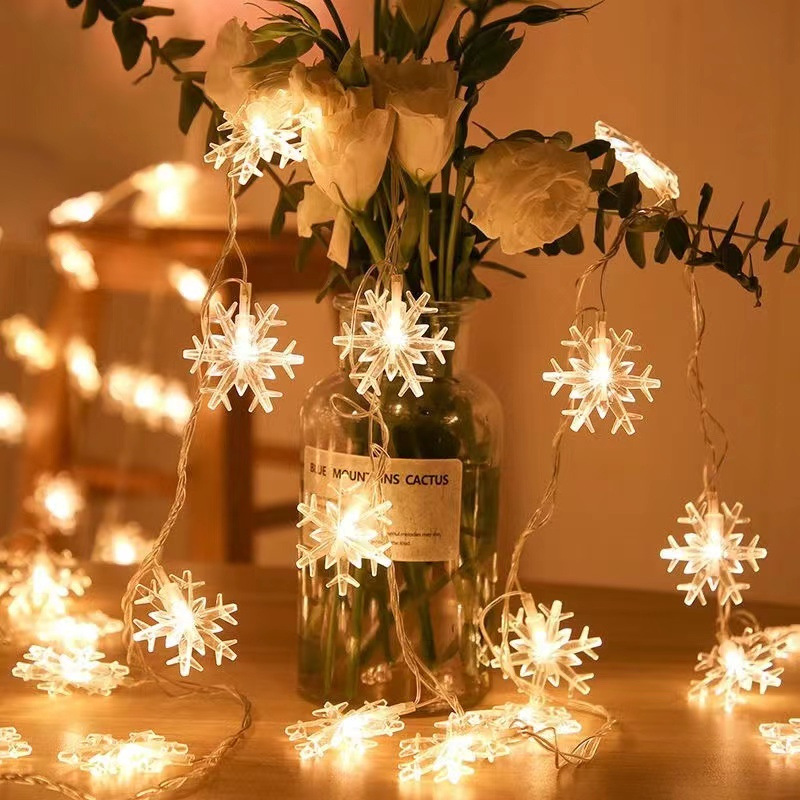 Światła w kształcie płatków śniegu w wazonie z białymi kwiatami. Światła są włączone i dają ciepły blask.