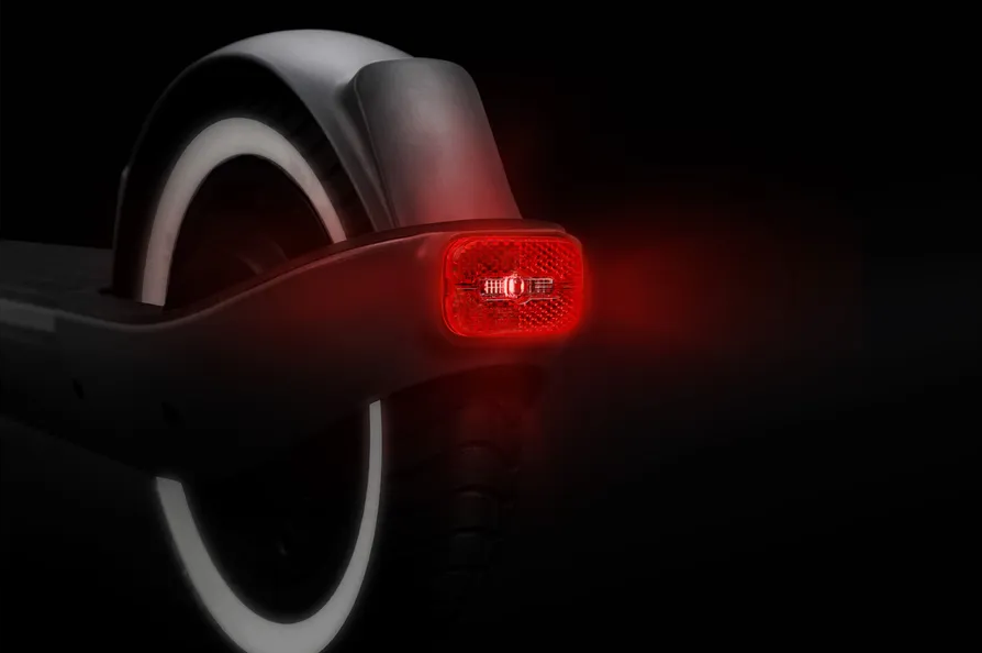 Primo piano della parte posteriore di un monopattino elettrico. La luce posteriore rossa si illumina. Pneumatico con bordo bianco. Lo sfondo è scuro.