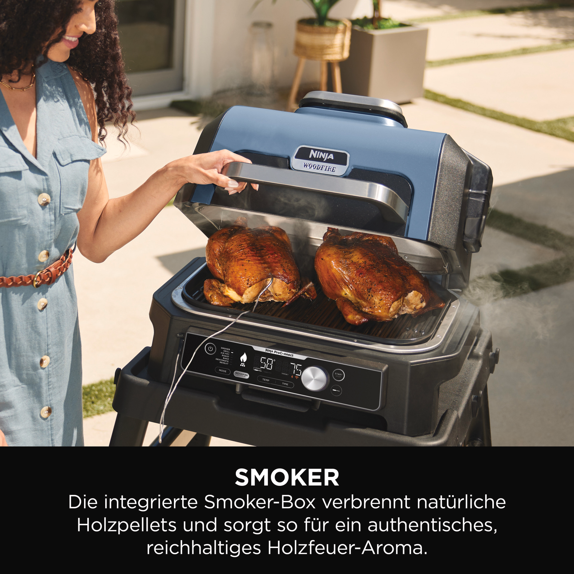 Ninja Woodfire Smoker mit zwei gegarten Hähnchen. Hand öffnet den Deckel.