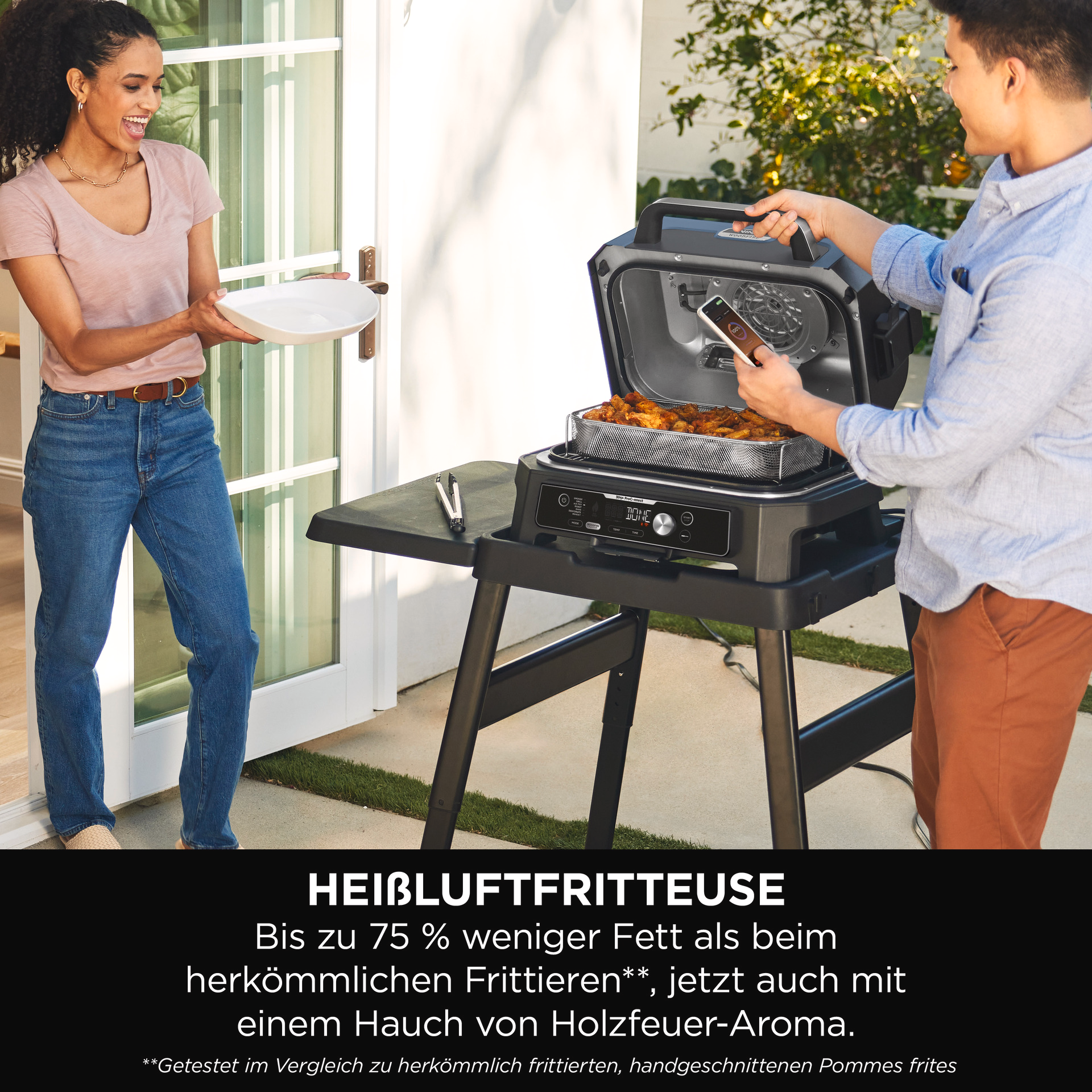 Zwei Personen benutzen einen Außengrill, der Text lautet 'Heißluftfritteuse'.