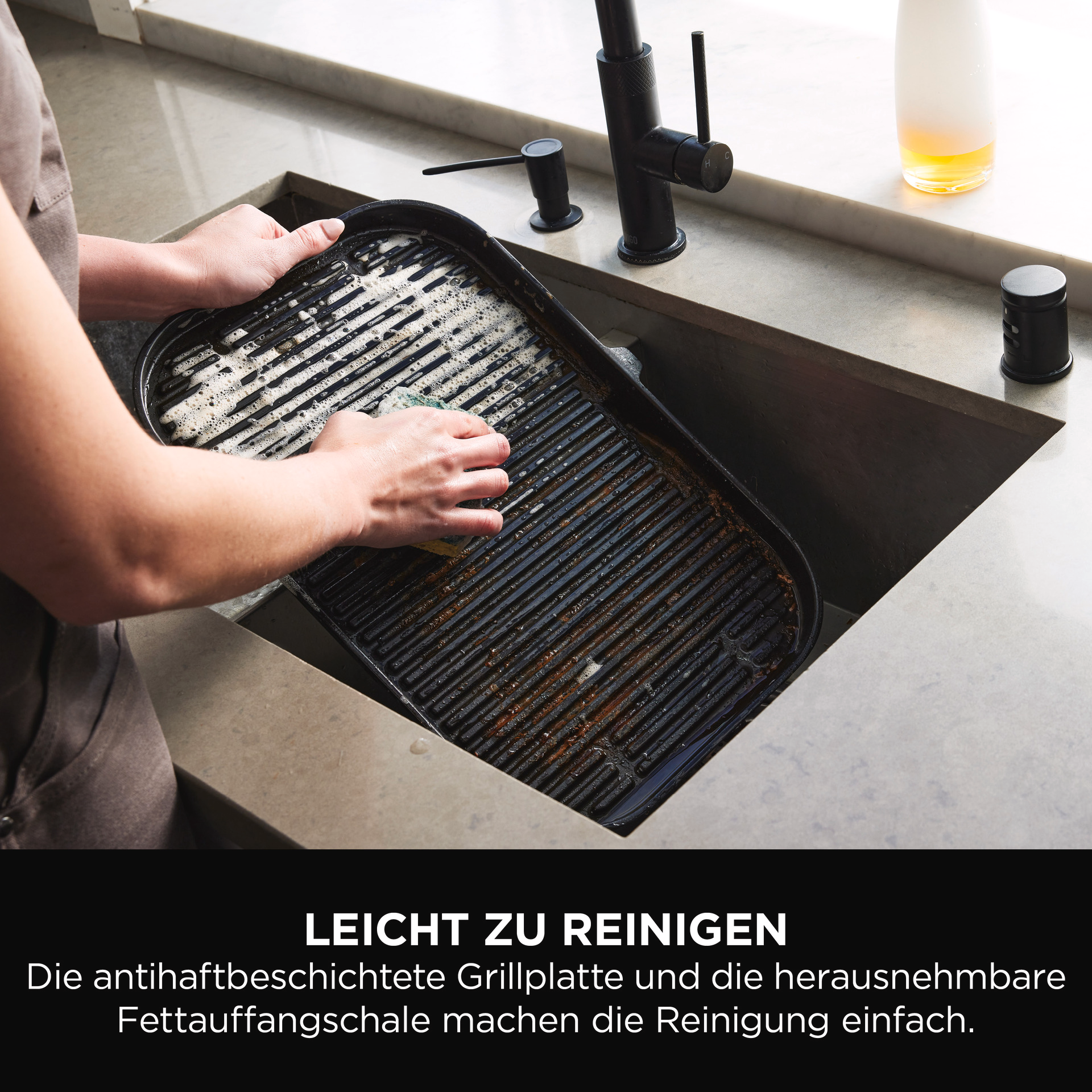 Person wäscht eine schwarze Grillpfanne in einem Waschbecken. Die Pfanne ist schmutzig.