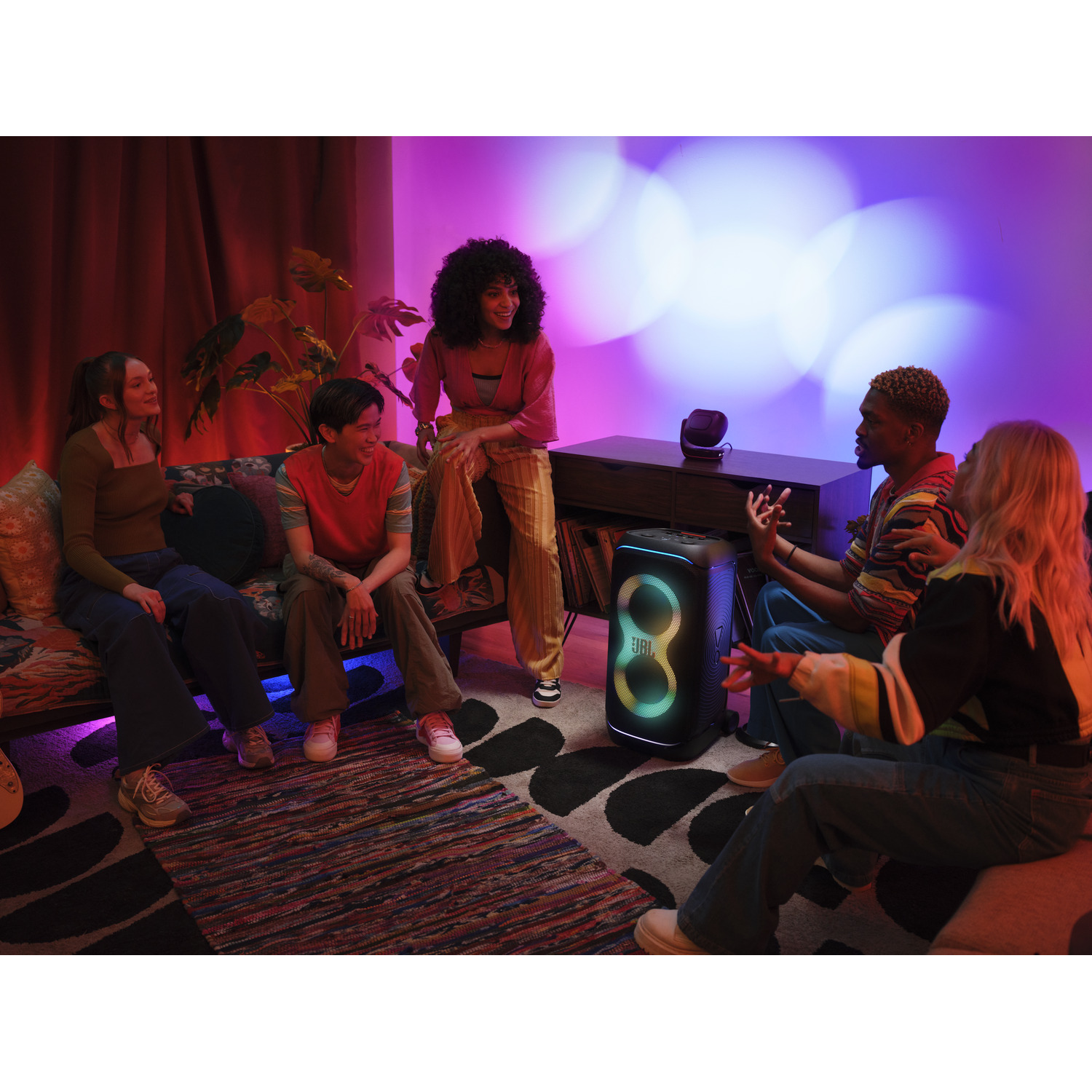Groep mensen met een speaker. Ze zijn in een kamer met kleurrijke lichten.