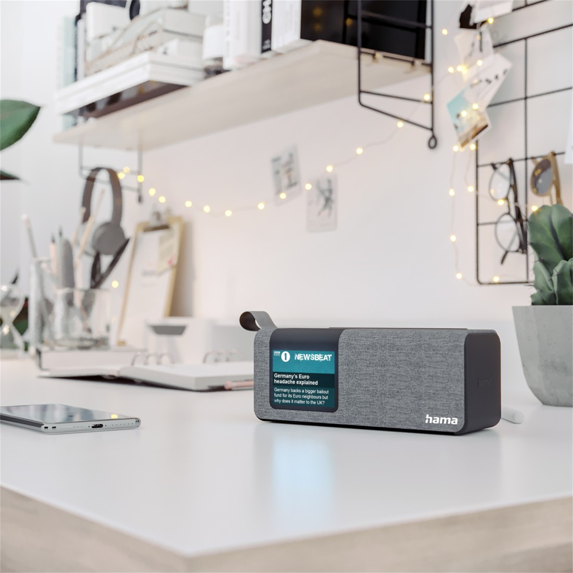 Un altavoz de radio con una pantalla que muestra noticias en un escritorio blanco.