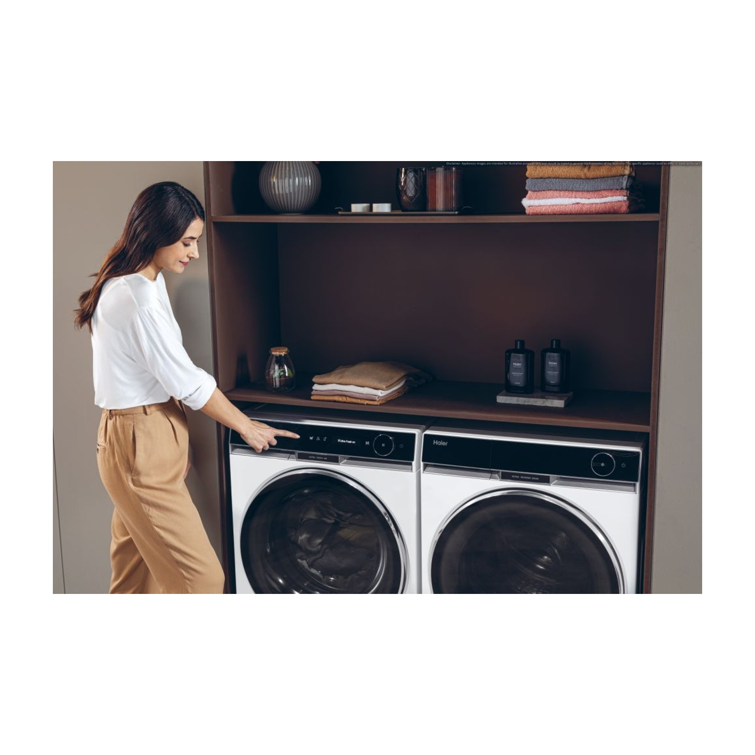 Donna con camicia bianca e pantaloni beige aziona una lavatrice bianca. Scaffali scuri sopra.