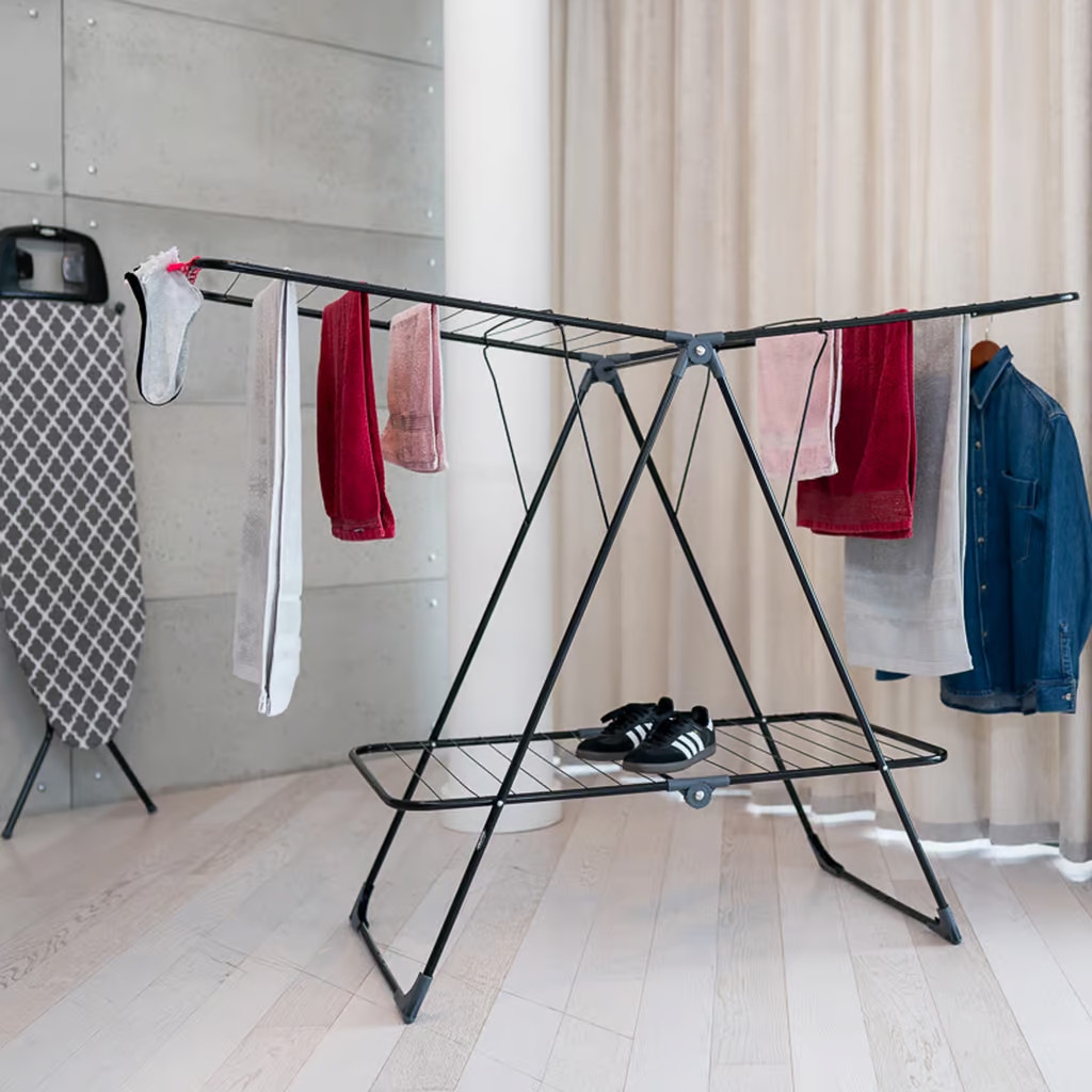 Suszarka do ubrań z wiszącymi ubraniami, deską do prasowania i parą butów.