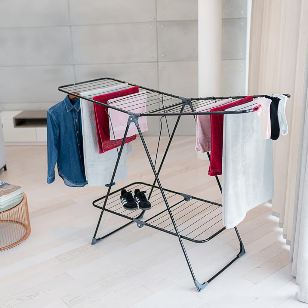 Suszarka do ubrań z wiszącymi ubraniami. Koszula dżinsowa, ręczniki i buty widoczne.