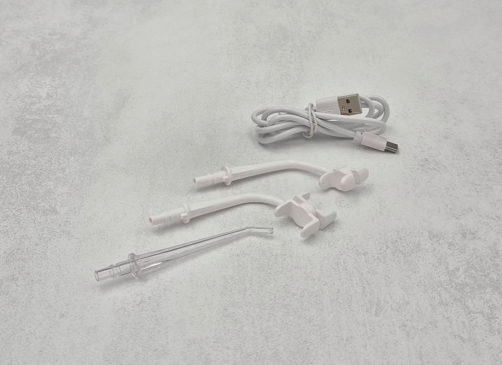 Weiße Zahnreinigungsgeräte: Aufsätze, ein Ladekabel und ein USB-A-auf-USB-C-Kabel.