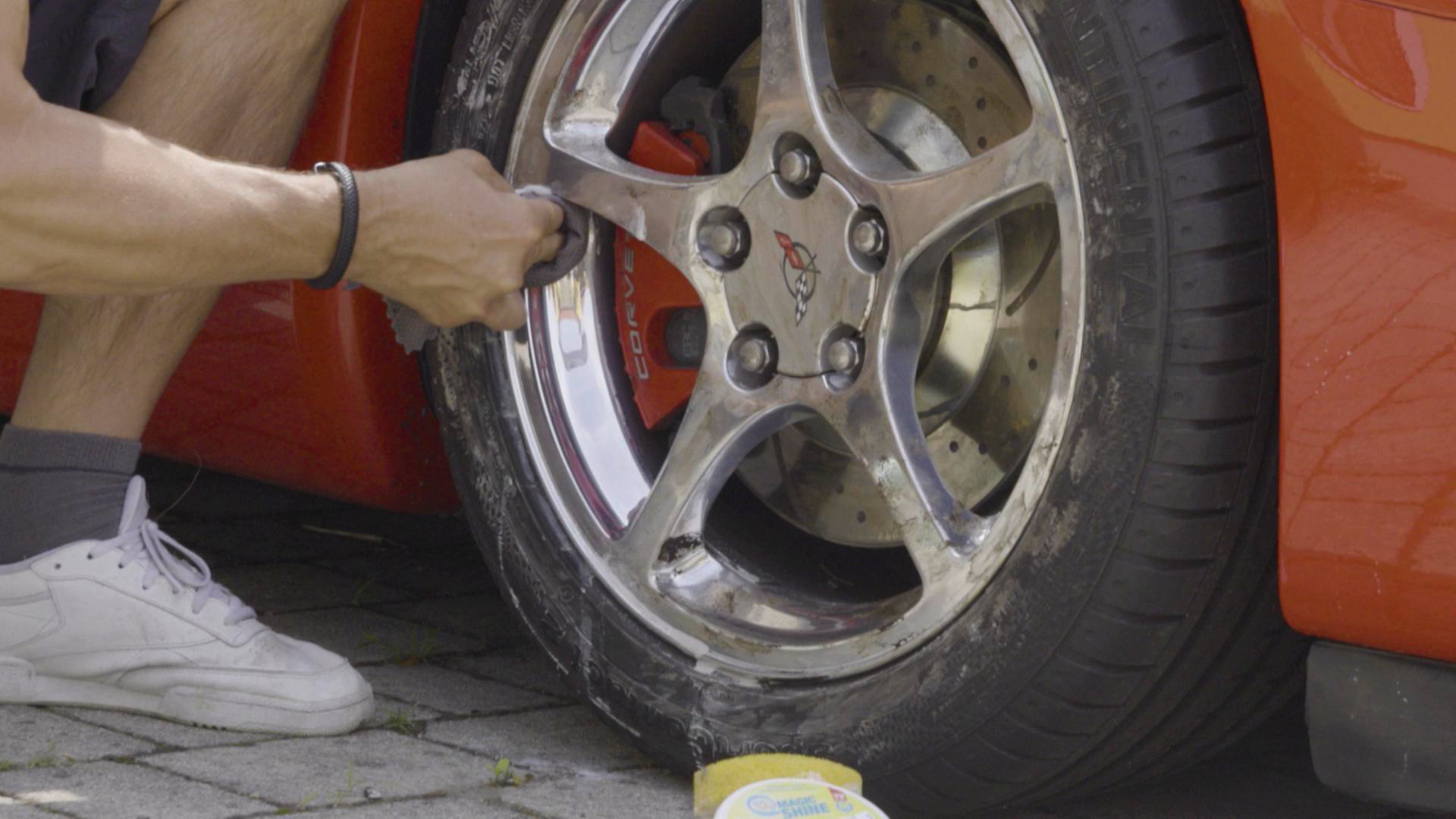 Eine Person reinigt ein Autorad mit einem Tuch und einem Schwamm. Das Auto ist rot.