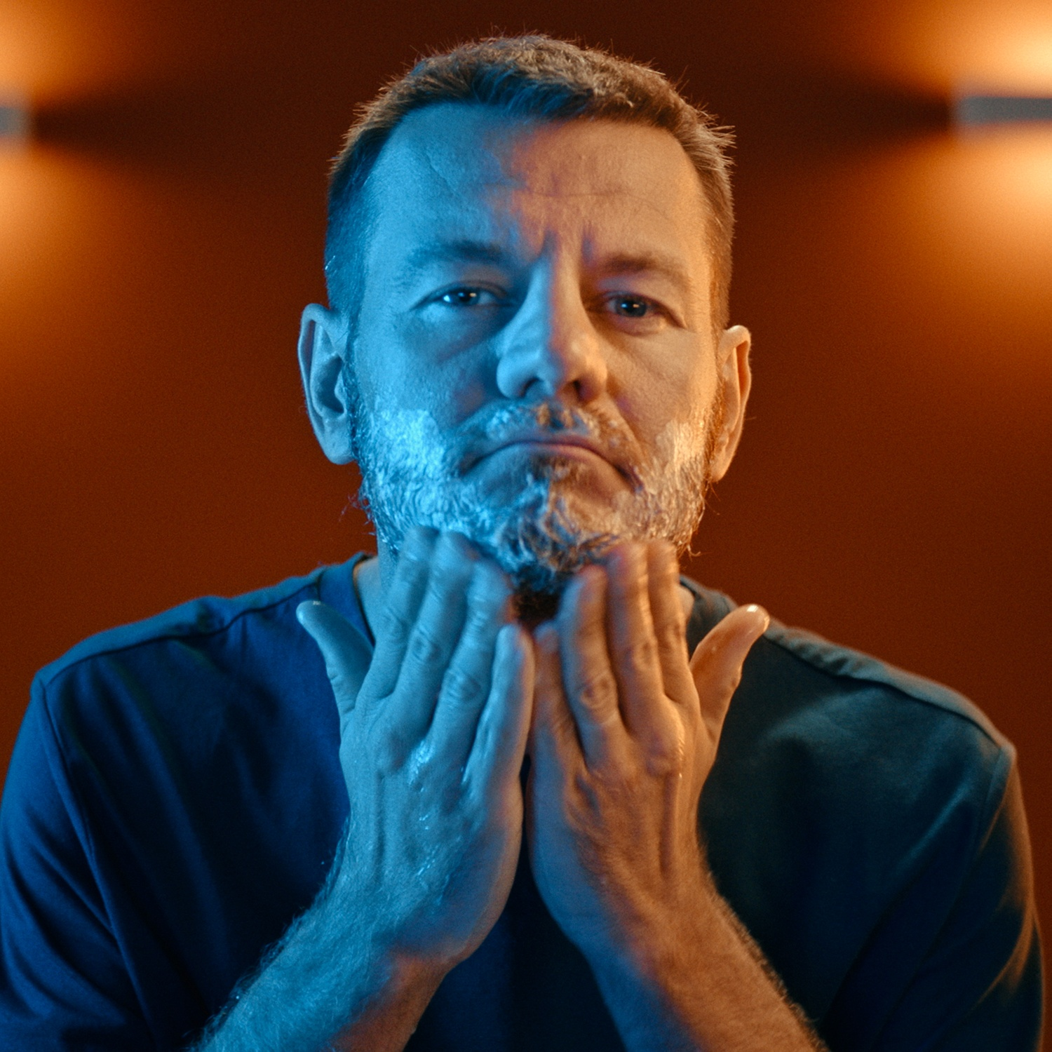 Uomo che applica la crema da barba. Guarda la fotocamera con espressione pensierosa.