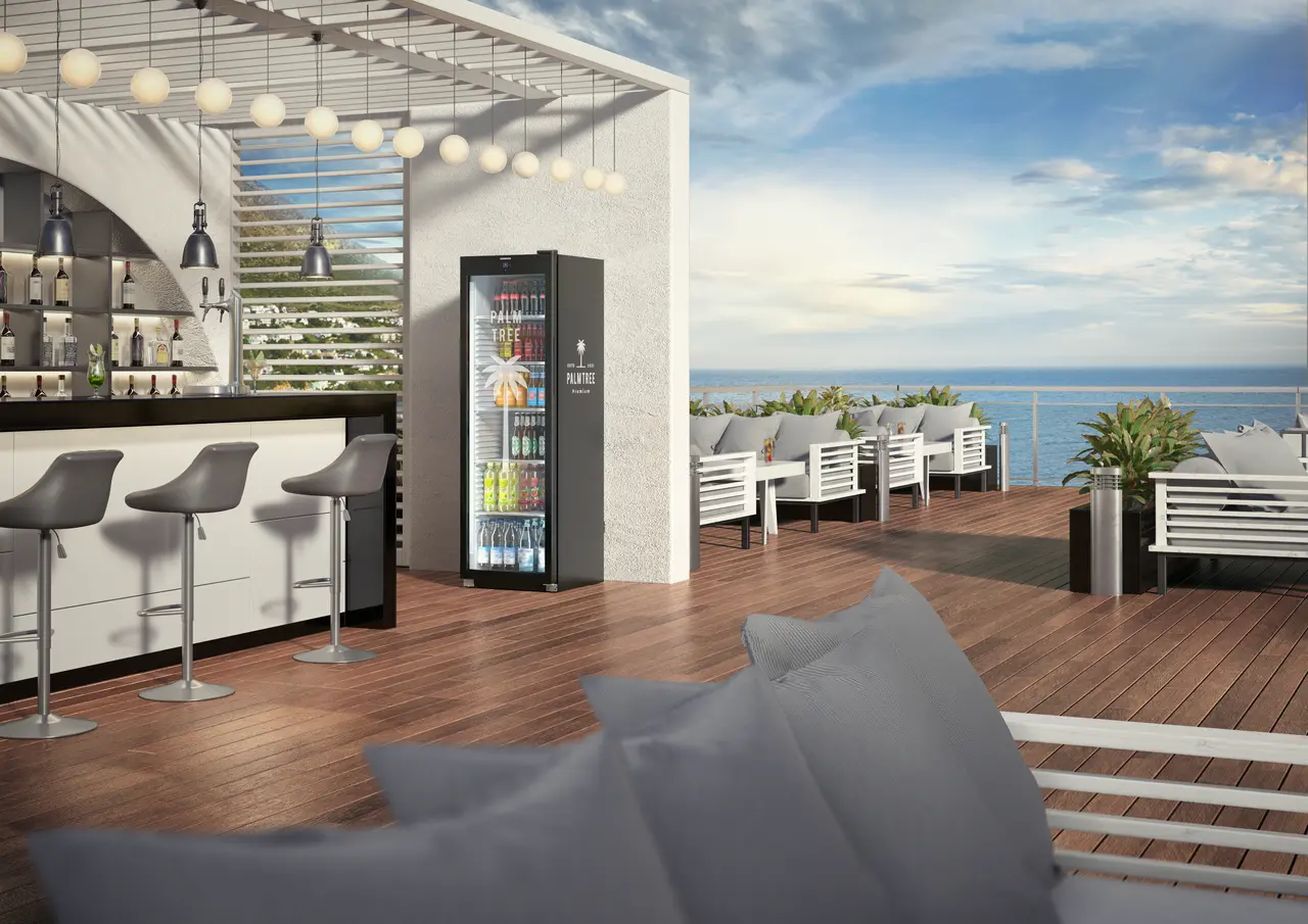 Szene einer Outdoor-Bar mit Meerblick. Kühlschrank, Bar und Sitzgelegenheiten sind sichtbar. Der Himmel ist blau.