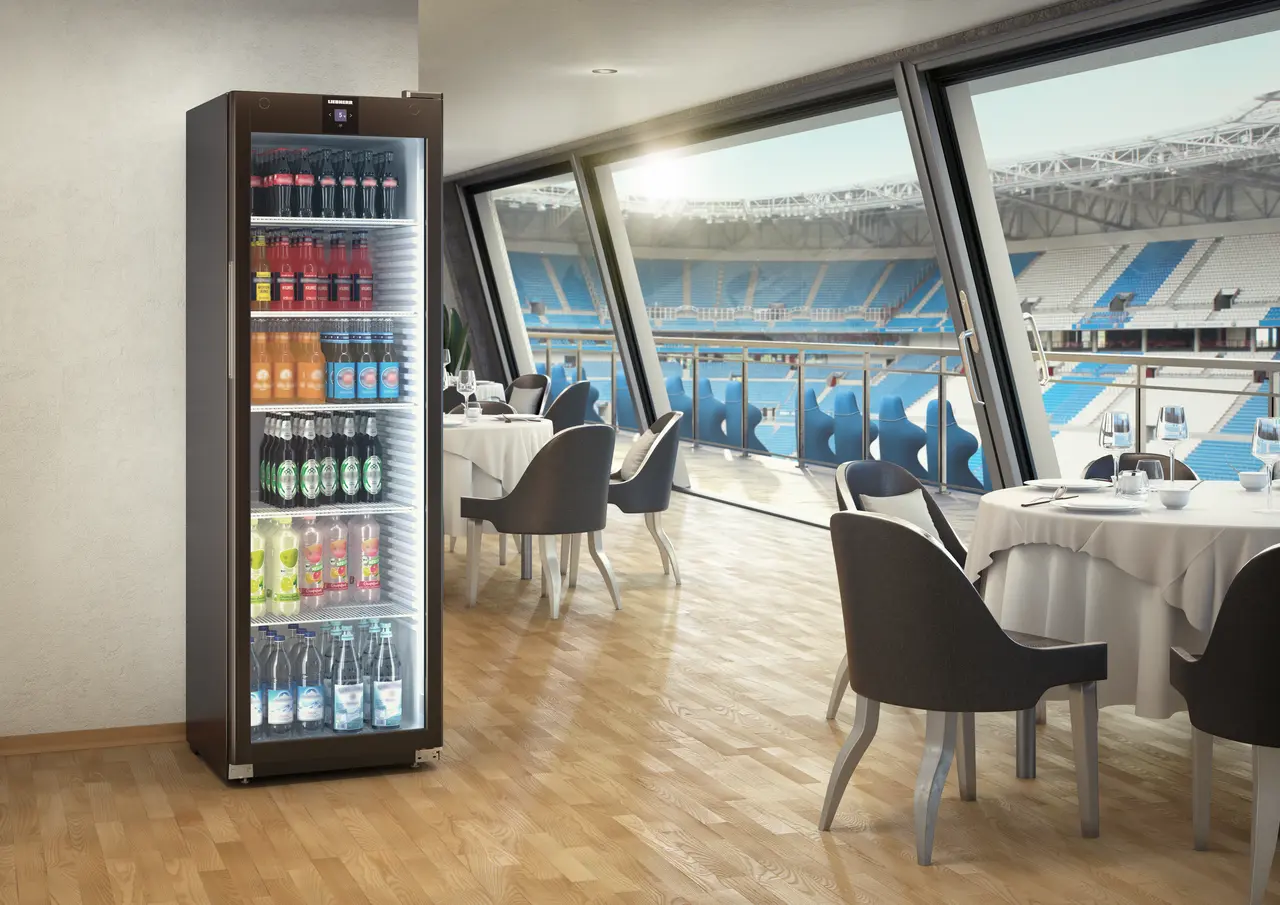 Ein Kühlschrank mit Getränken. Im Hintergrund ein Restaurant mit Stadionblick.