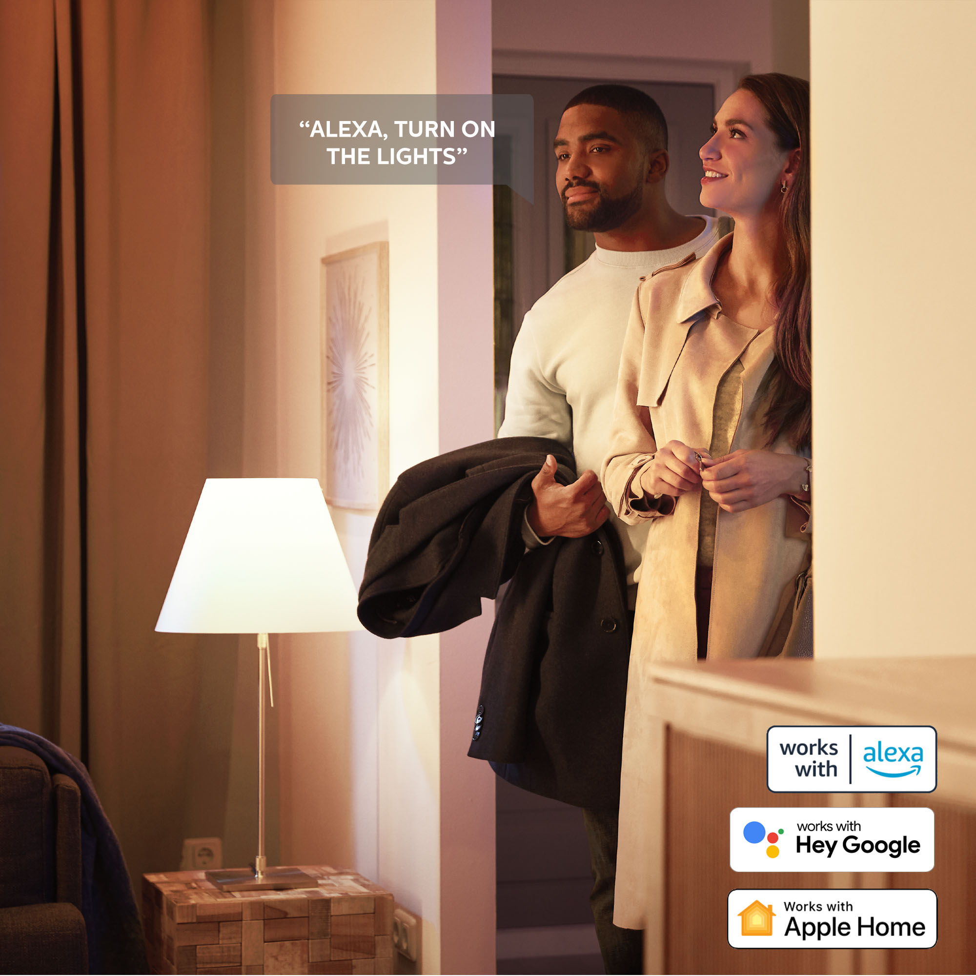 Ein Paar in einem Raum, mit einer Tischlampe und einer Textblase mit „ALEXA, SCHALT DAS LICHT EIN“.