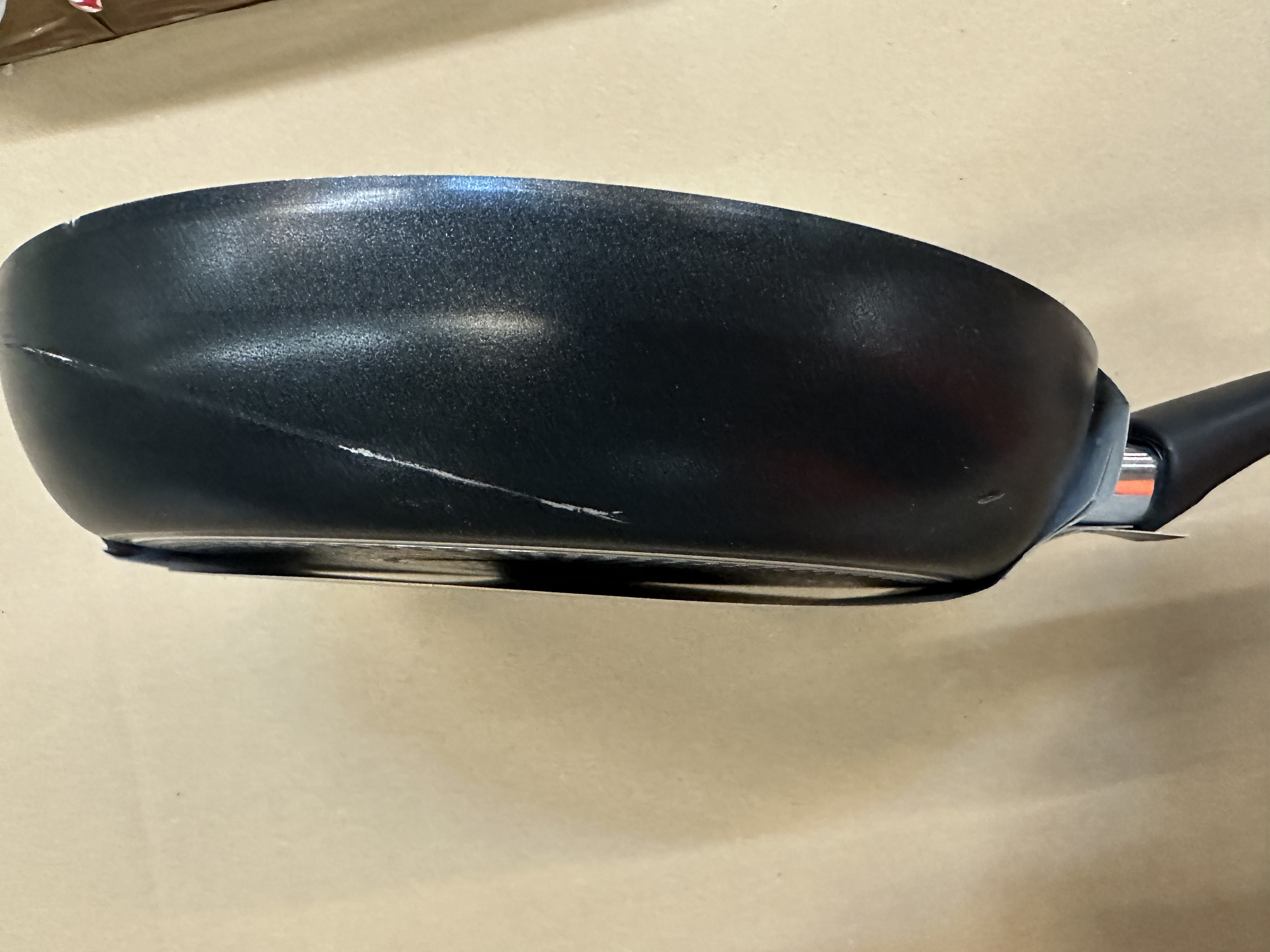 Czarna patelnia z uchwytem, pokazująca zarysowania na boku.