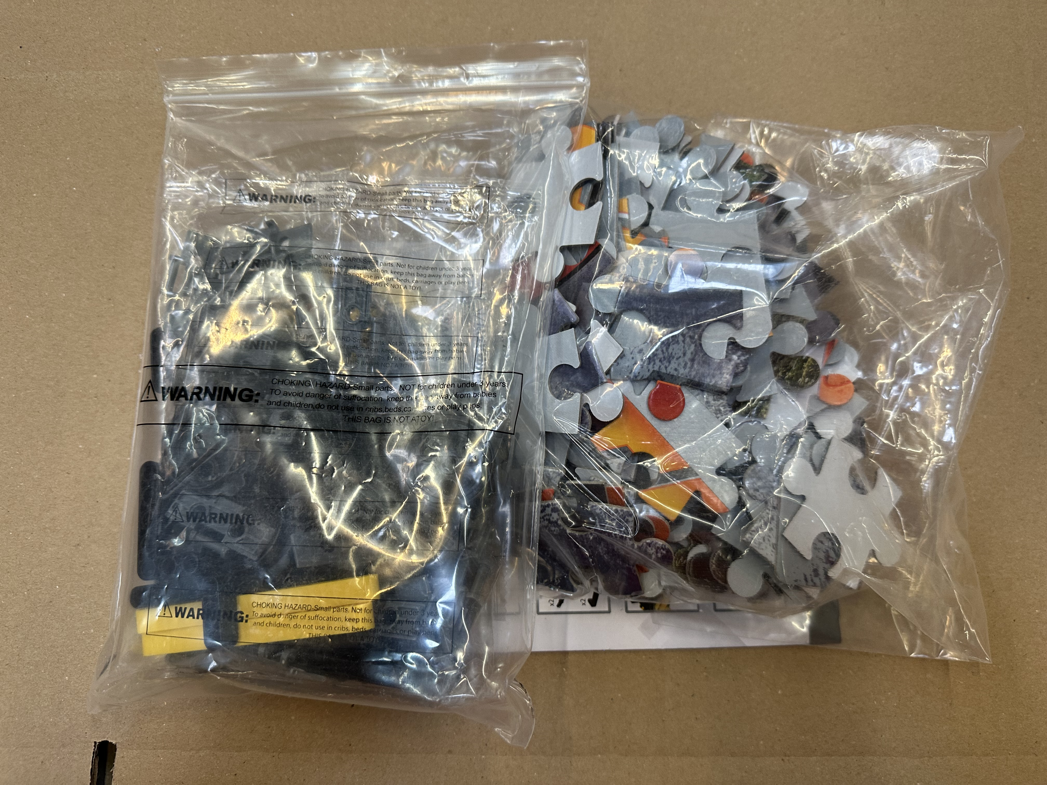 Dwie plastikowe torby z elementami puzzli w środku. Jeden ma czarne elementy, drugi kolorowe.