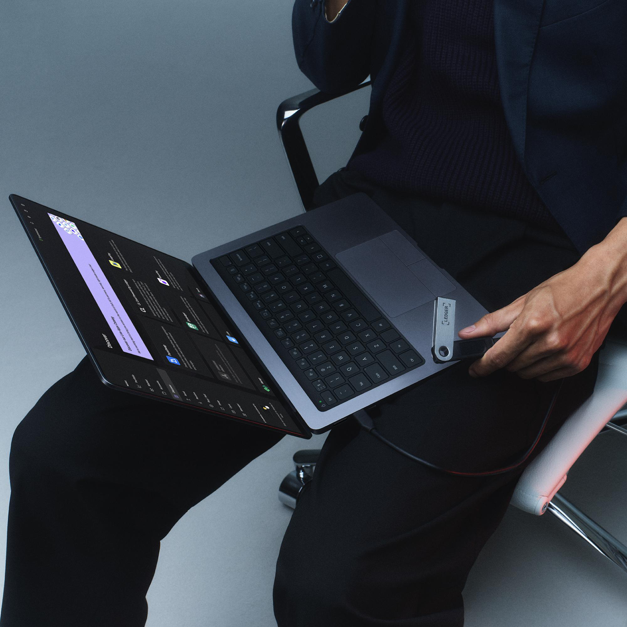 Eine Person hält einen Laptop, offen, mit schwarzer Tastatur, sitzt auf einem Stuhl.