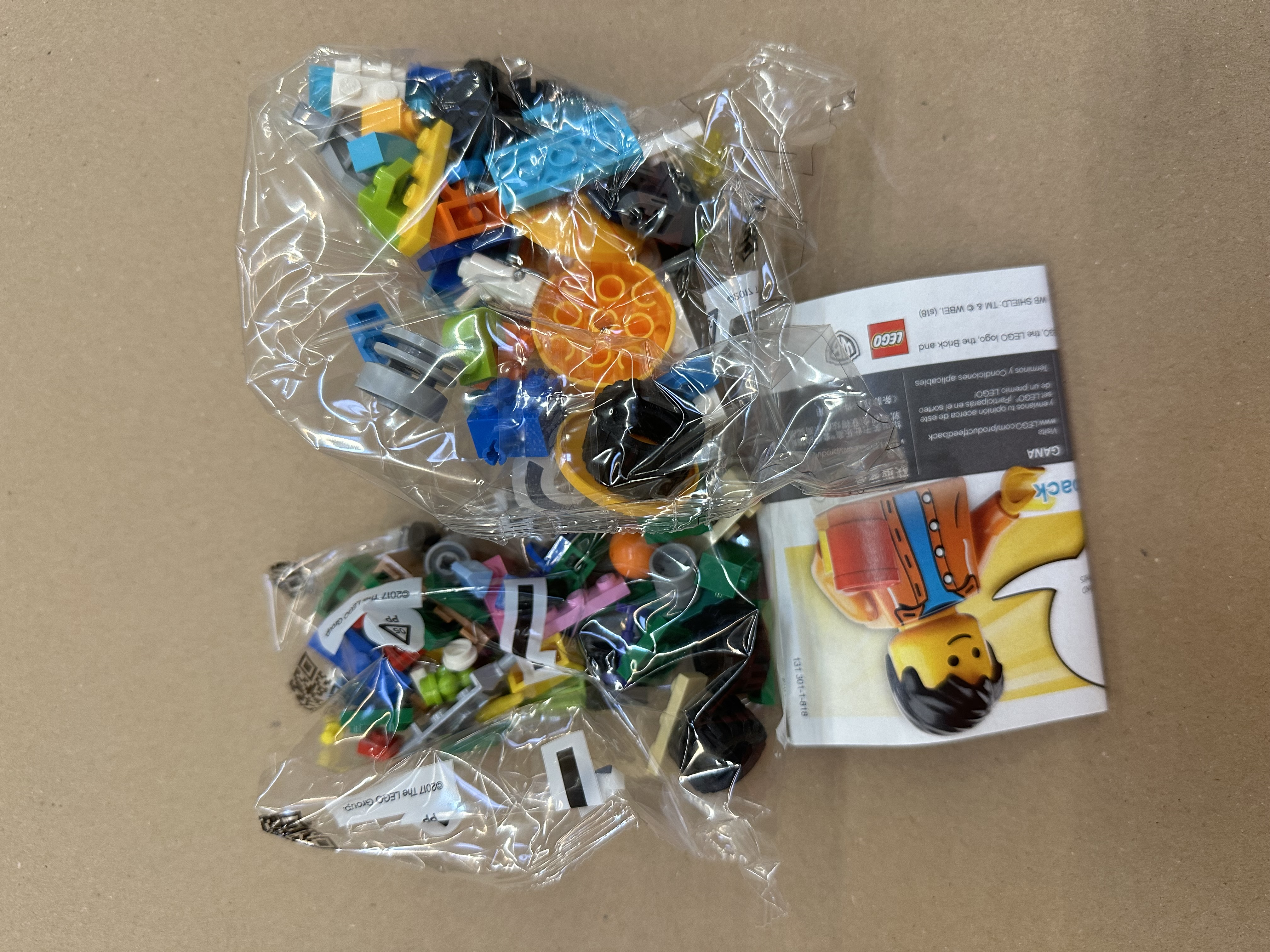 Dwa plastikowe worki z kolorowymi klockami LEGO i instrukcjami. Jeden worek na górze, drugi na dole.