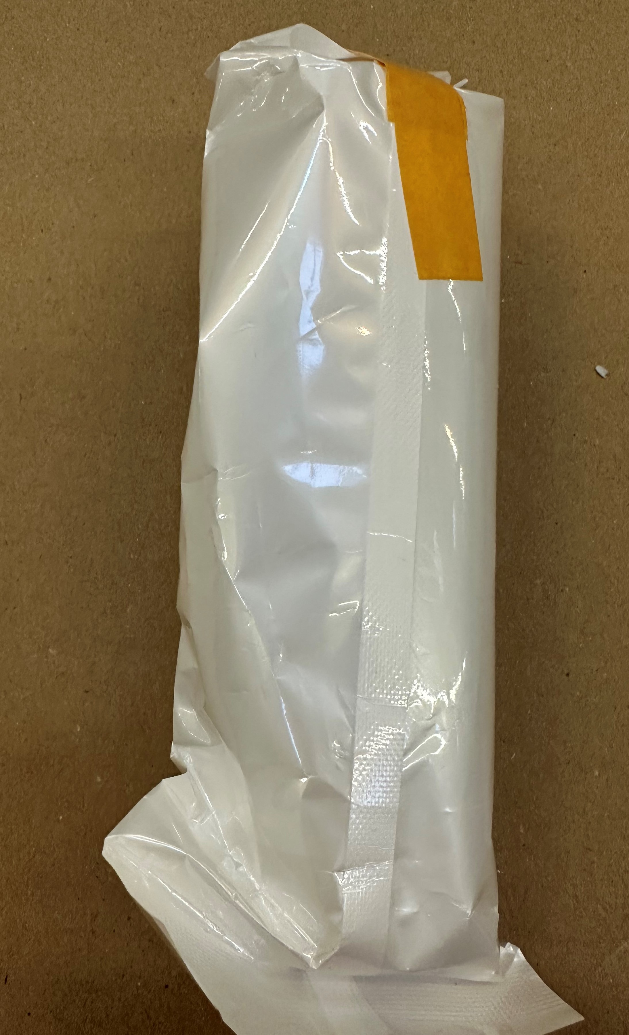 Biała plastikowa paczka z pomarańczową taśmą na brązowej powierzchni.