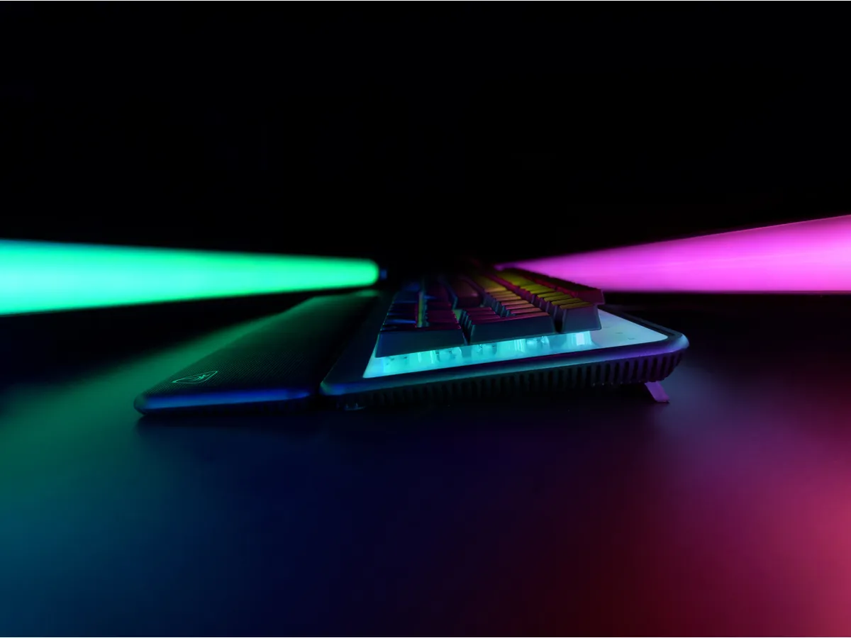 Eine Tastatur mit einer Handauflage, beleuchtet mit grünen und pinkfarbenen Lichtern, vor schwarzem Hintergrund.