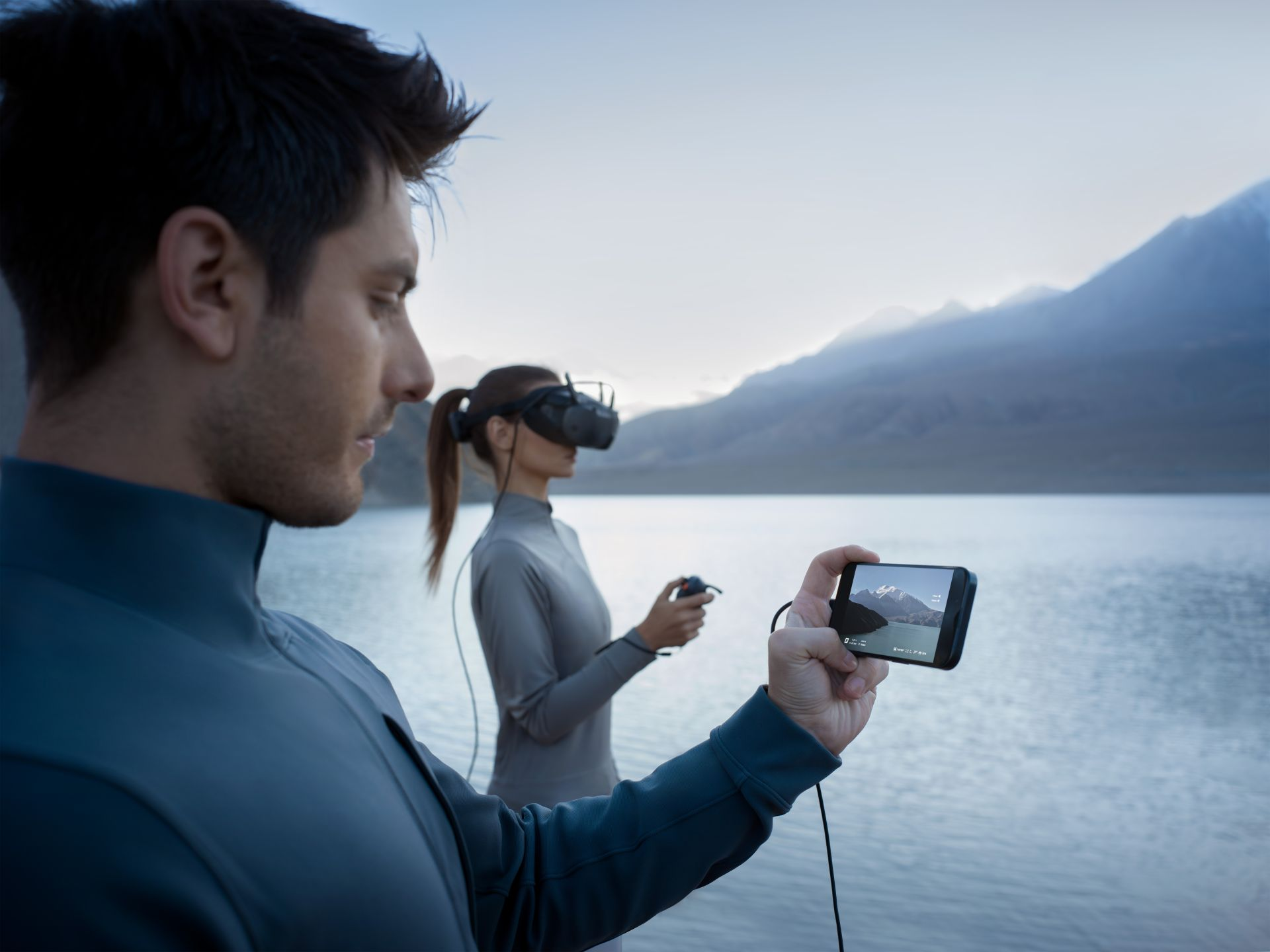 Eine Person hält ein Telefon mit einem Bild, während eine andere VR-Brille trägt.