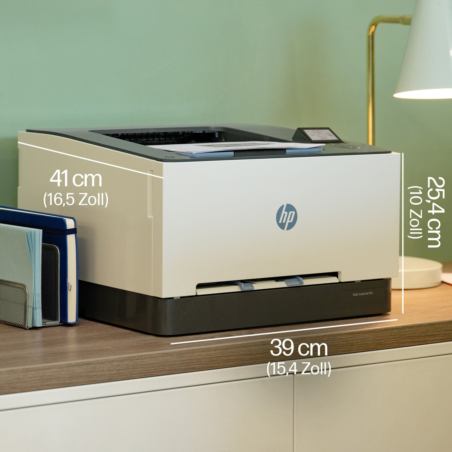 Imprimante HP noire et blanche sur un bureau. Dimensions indiquées. Classeurs bleus et lampe en arrière-plan.