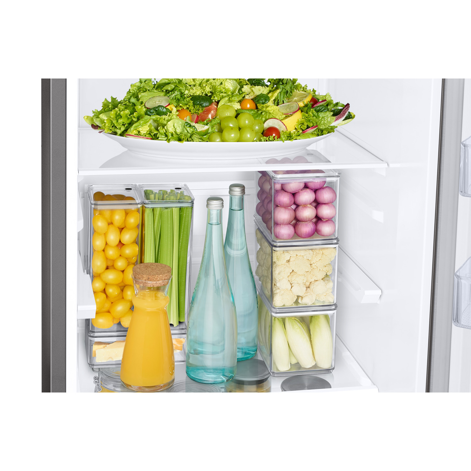 Inside a refrigerator with food. Includes a salad, bottles of water, juice and vegetables.