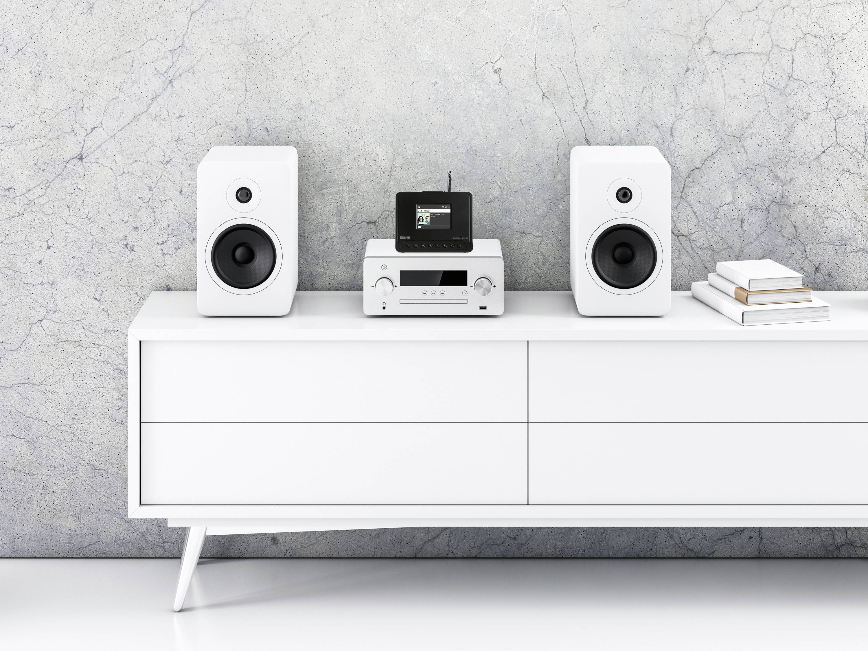 Meuble TV blanc avec deux enceintes blanches, un lecteur CD et des livres. Fond de mur gris.