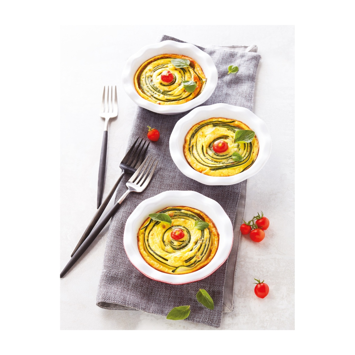 Tre quiche con pomodorini e foglie di basilico su un tovagliolo grigio.