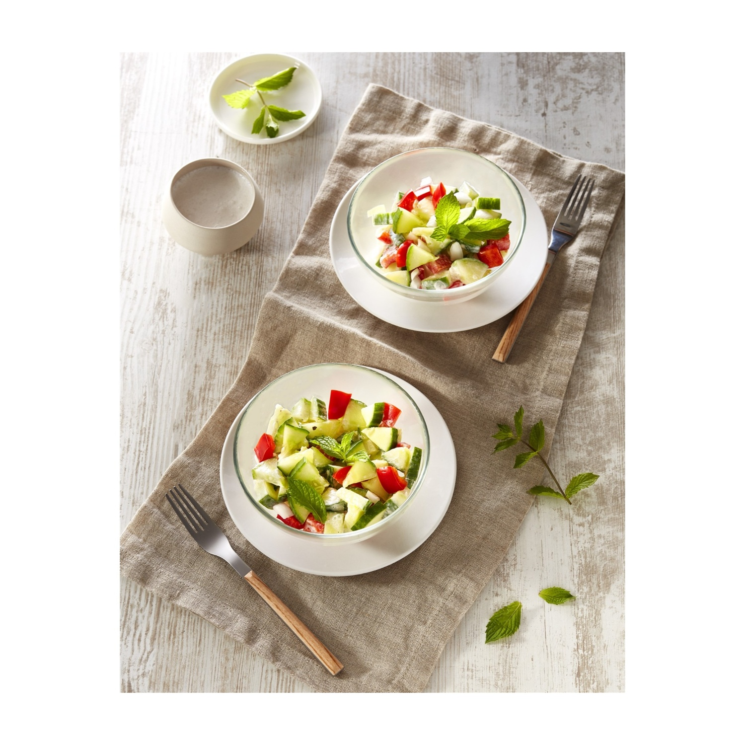 Insalata con cetrioli, pomodori e menta servita in ciotole su tessuto di lino. Due forchette.