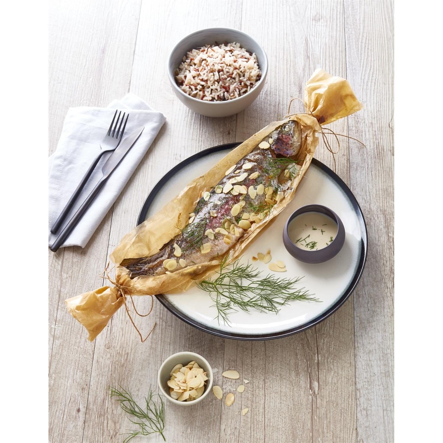 Pesce al forno in carta forno, servito con riso, salsa e mandorle.