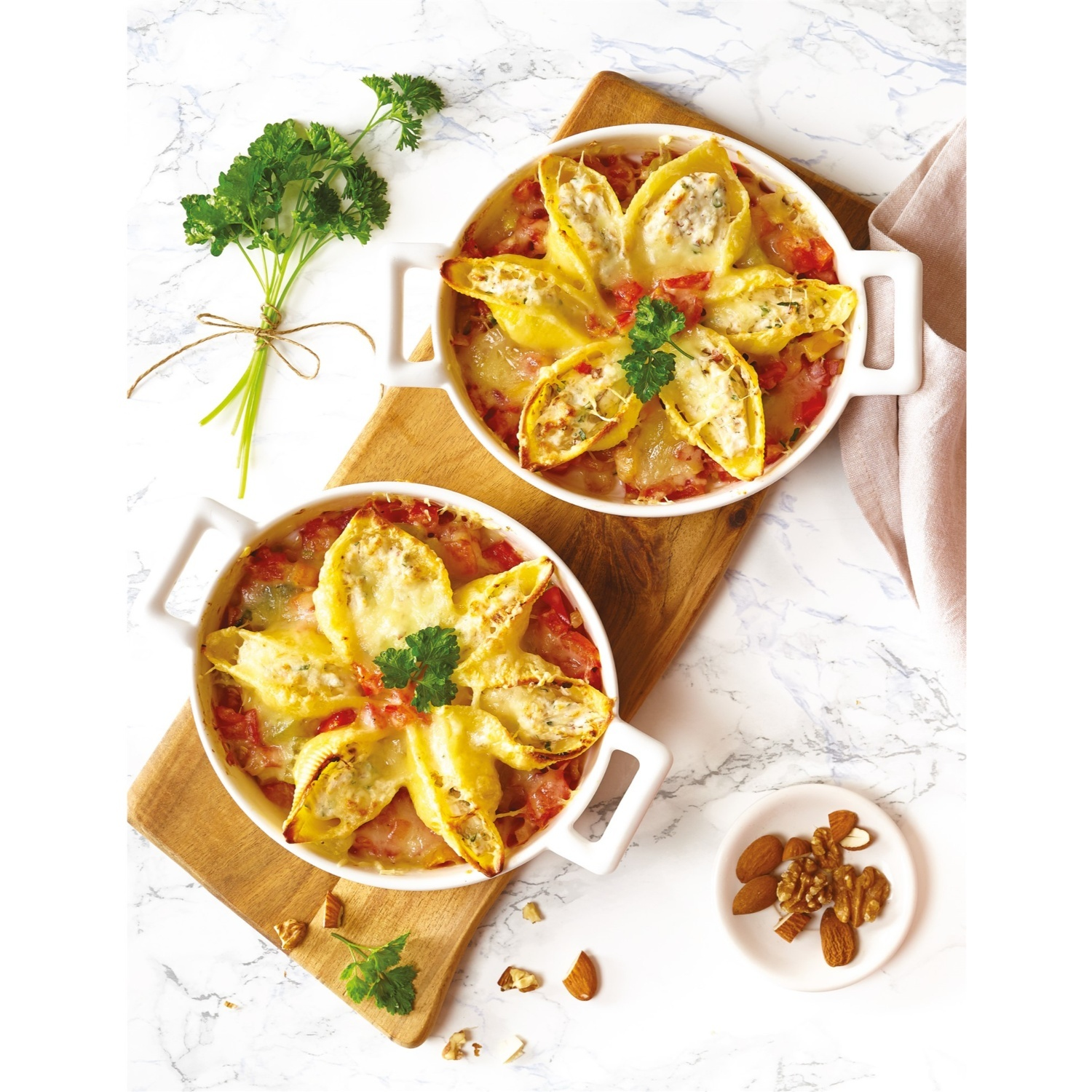 Due piatti di pasta con formaggio e prezzemolo, mandorle e noci su un tagliere di legno.